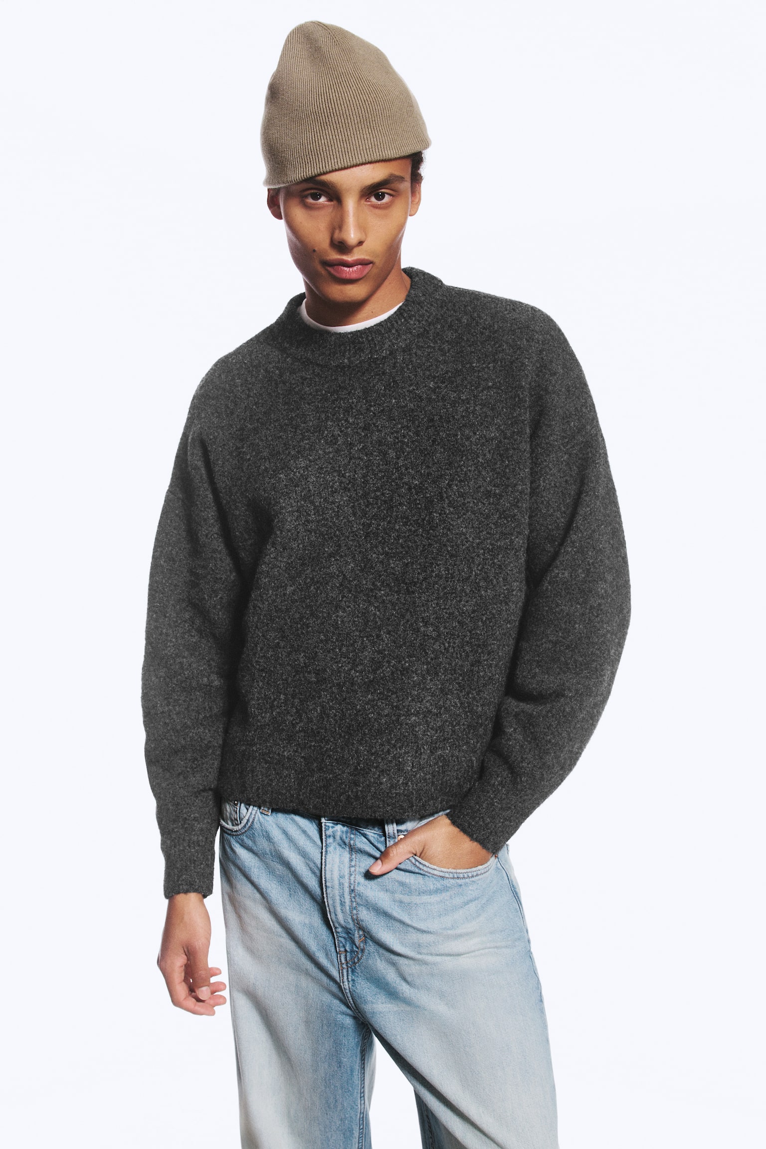 En mørkegrå genser i ullblanding med avslappet passform, senkede skuldre og ribbestrikkede kanter bæres av modellen. Genseren er lagdelt over en hvit T-skjorte og kombinert med lyseblå jeans i lys vask. - 1