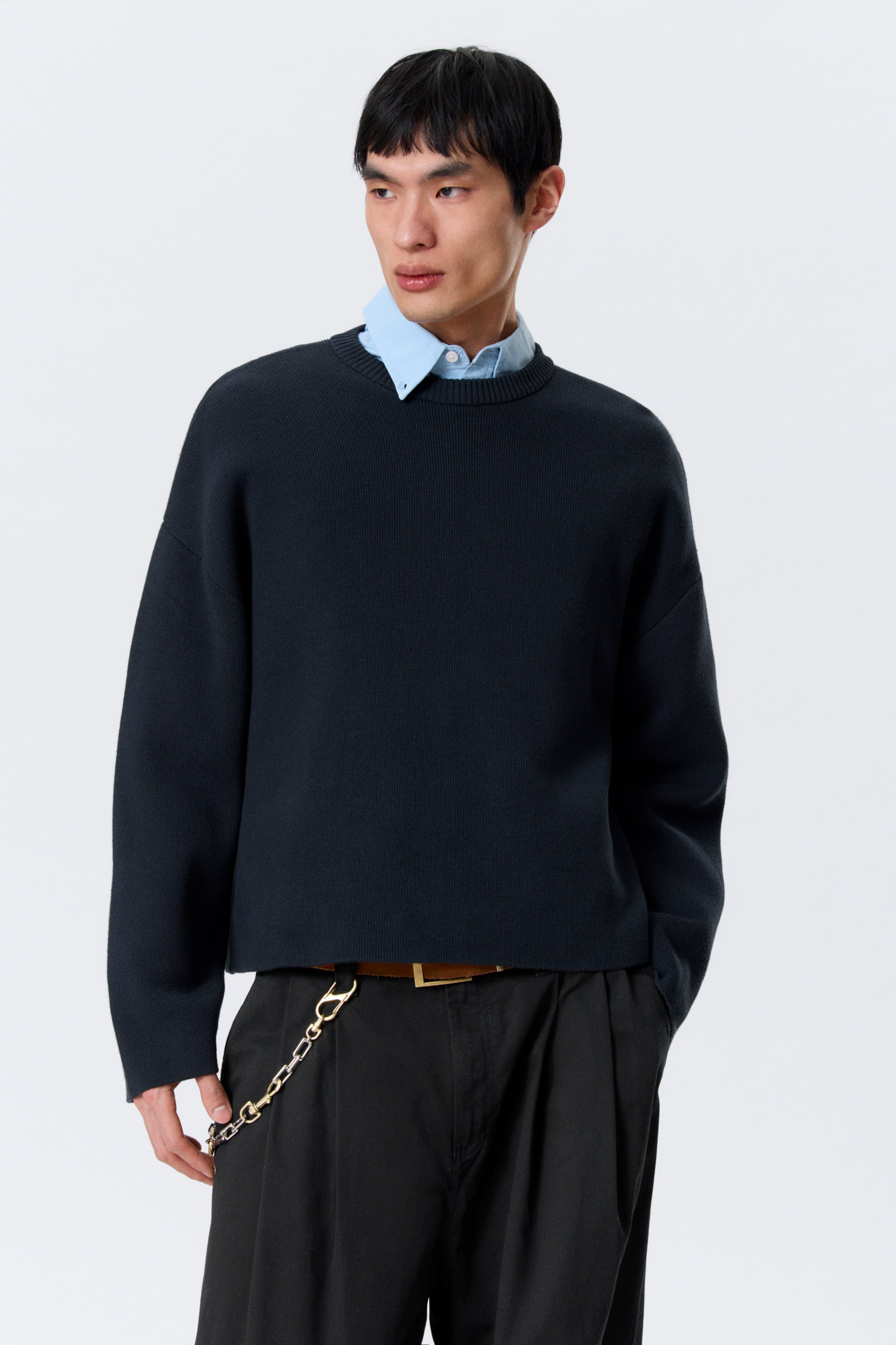 Agrandir l'image: Le pull à col rond bleu foncé est présenté de face, avec une coupe décontractée aux épaules tombantes, des manches longues et un ourlet côtelé court. Une chemise à col bleu clair est visible sous son col rond côtelé.