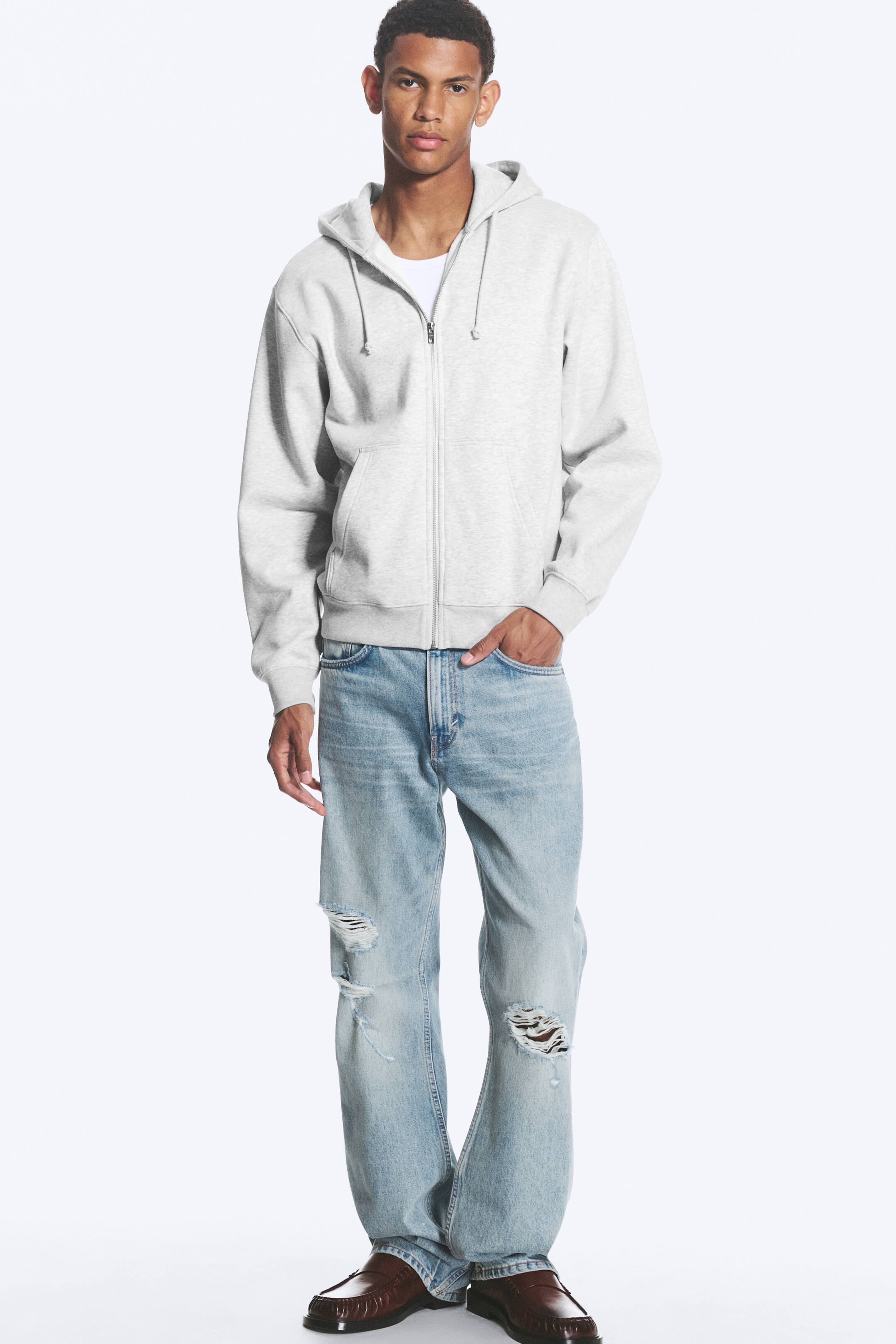 Visa större bild: En ljusgrå hoodie med hel dragkedja visas framifrån och har en fastsydd huva med synliga dragsnören, kängurufickor samt ribbade muddar och nederkant. Den bärs öppen över en vit t-shirt.
