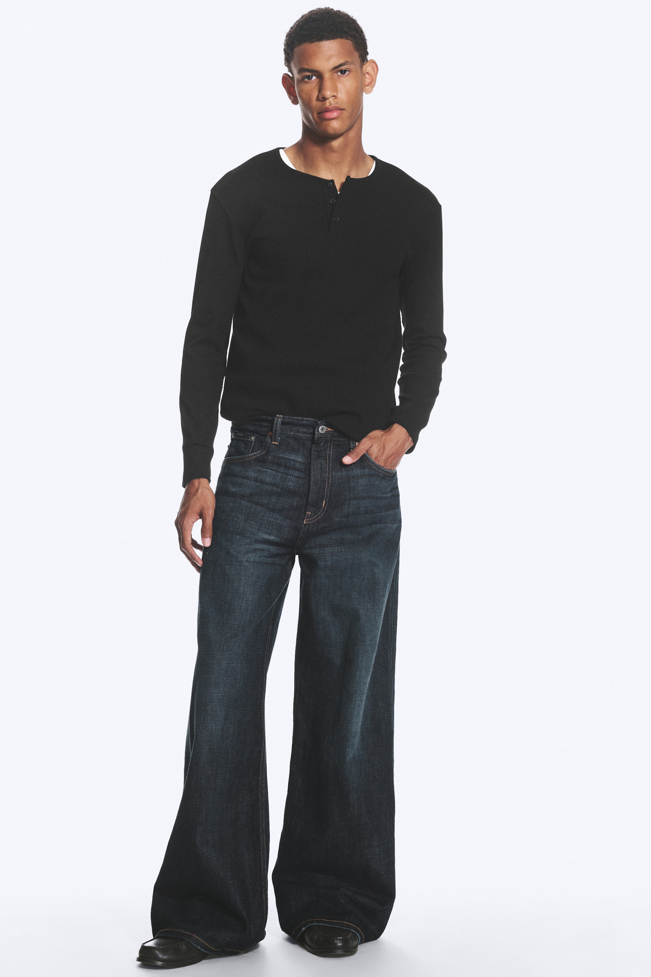 Visualizza l'immagine ingrandita: Jeans a lavaggio scuro, vestibilità ampia con vita media e gamba larga indossati dalla modella. I jeans presentano un design a cinque tasche e cuciture visibili, e la modella ha una mano infilata in una tasca anteriore.