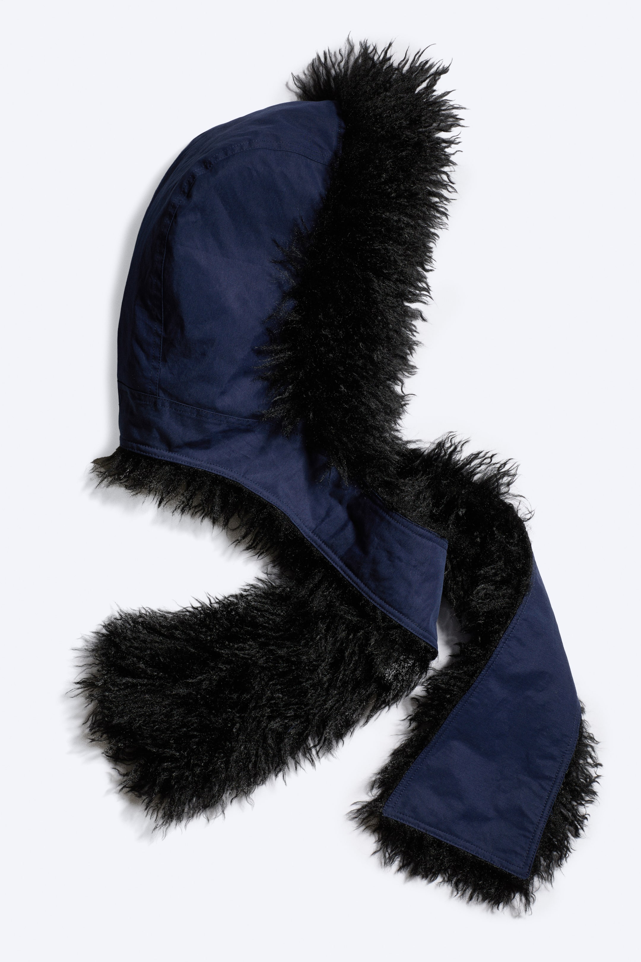 Grotere afbeelding bekijken: Faux bont capuchonsjaal. Het product heeft een marineblauwe capuchon afgezet met ruig zwart imitatiebont, dat doorloopt om de aangehechte sjaaldelen te bekleden. De sjaaldelen hebben een marineblauwe stoffen buitenkant.