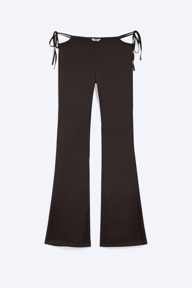 Pantalones marrón oscuro que presentan una cintura alta con secciones recortadas distintivas en las caderas, cada una con cordones decorativos atados. Los pantalones están diseñados con un tejido de punto texturizado sutil y se ensanchan ampliamente desde la rodilla hasta el dobladillo. - 1
