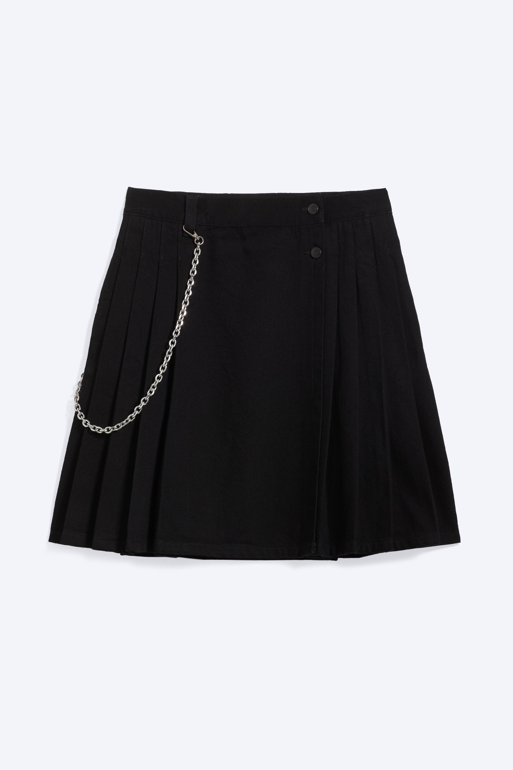 View larger image: A black pleated, wrap-style skirt is facing front, featuring a silver-coloured chain attached to a waistband loop. Two black buttons are securing the skirt's front closure.