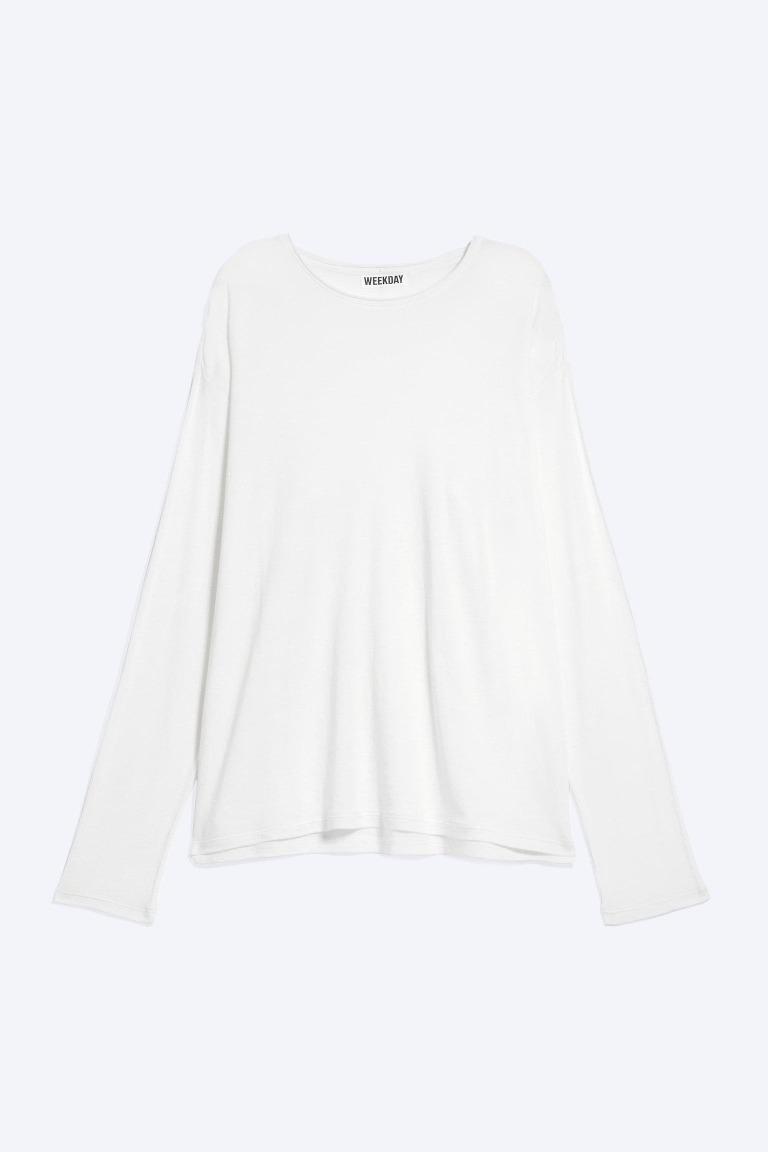 Una maglia bianca a maniche lunghe presenta la vista frontale, caratterizzata da uno scollo rotondo e maniche lunghe e dritte con orli semplici. Il nome del marchio "WEEKDAY" è visibile su un'etichetta nera sul retro del collo.