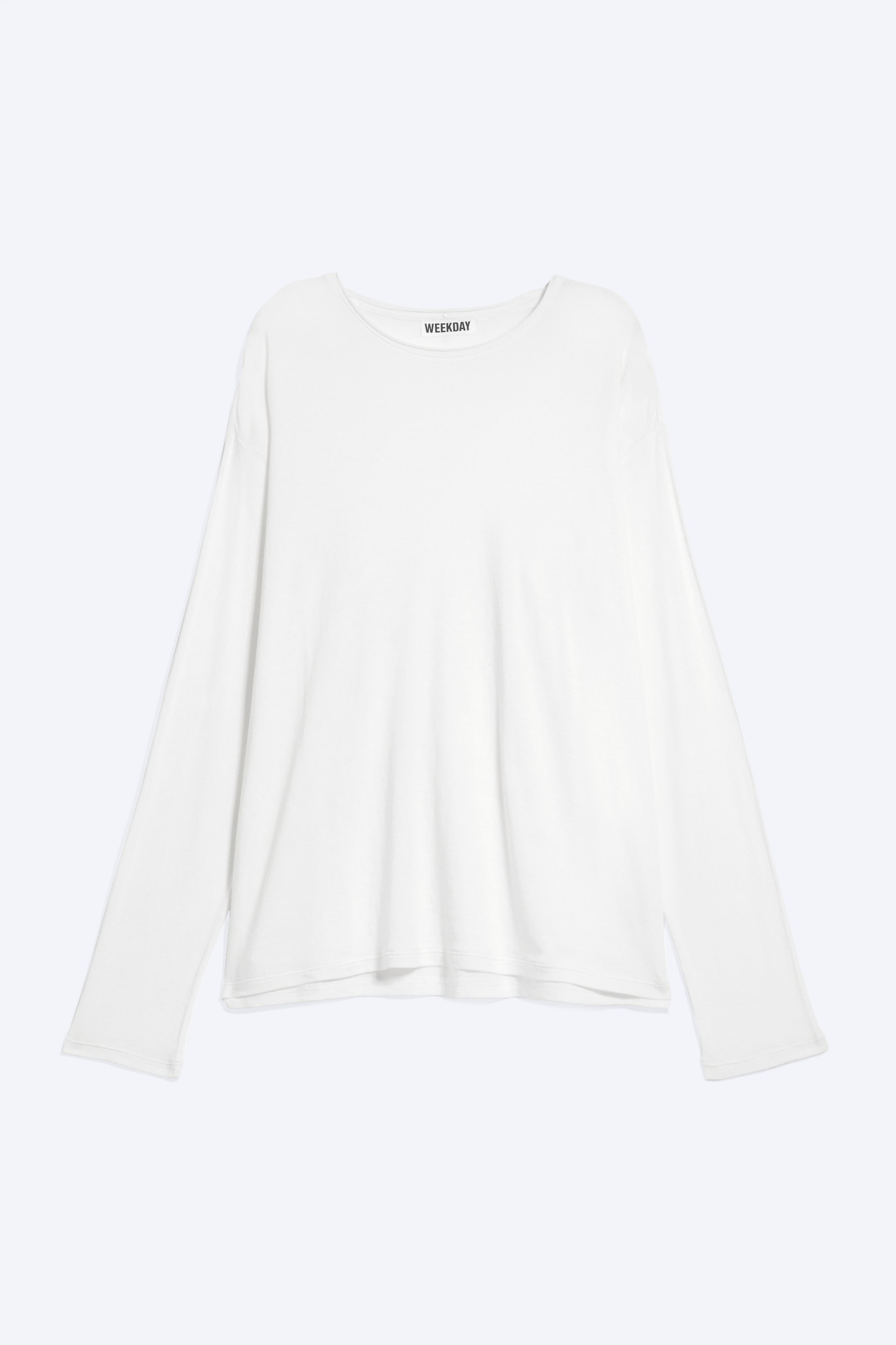 Größeres Bild anzeigen: Ein weißes Langarmshirt präsentiert seine Vorderansicht, mit einem runden Halsausschnitt und langen, geraden Ärmeln mit einfachen Säumen. Der Markenname "WEEKDAY" ist auf einem schwarzen Etikett am hinteren Halsbereich sichtbar.