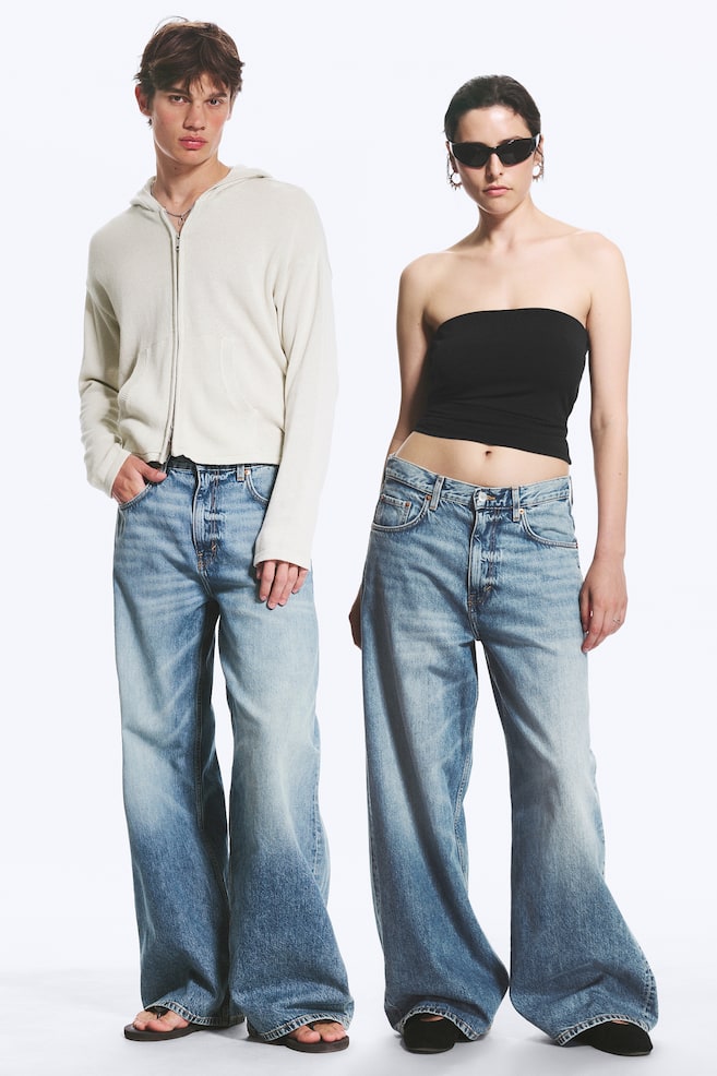 Blugii cu croială largă și spălare deschisă sunt realizați dintr-un denim albastru decolorat, cu un efect de gradient, trecând de la un albastru mai deschis la coapse la un albastru mai închis la tiv. Sunt concepuți cu o siluetă relaxată și largă, având o închidere vizibilă cu nasturi, care subliniază un croi lejer. - 1