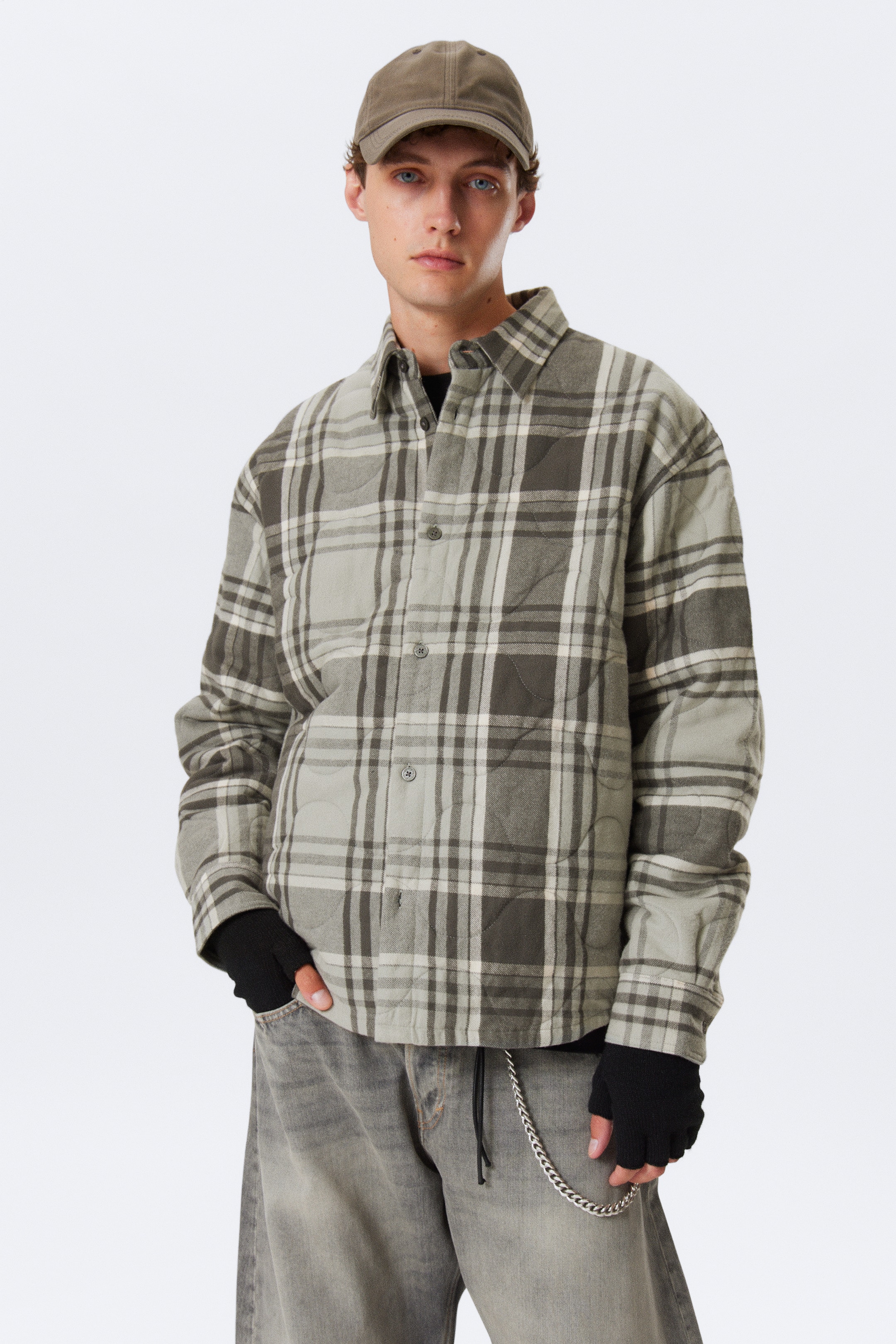 Vis større bilde: En quiltet rutete skjortejakke presenteres forfra, med et stort grått og off-white rutemønster med diamantquilting. Den er designet med en spiss krage, en knappelukking foran, to brystlommer og knappede mansjetter, og har en avslappet passform.