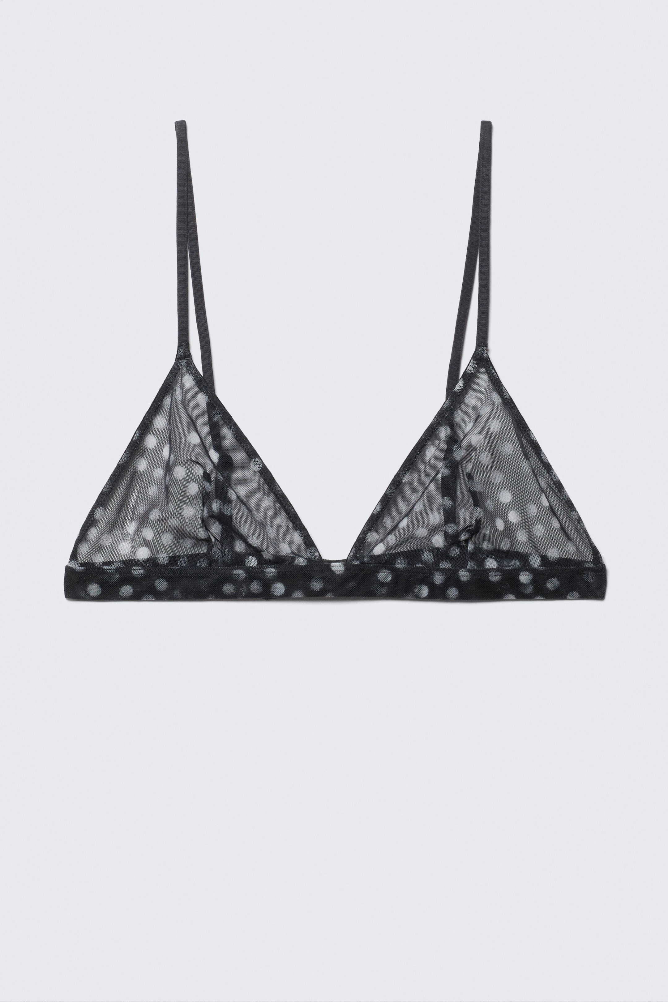 Ver imagen más grande: Un bralette triangular negro de encaje transparente está orientado hacia el FRENTE, mostrando lunares blancos a lo largo de su tela. Presenta finos tirantes tipo espagueti y una banda elástica visible debajo.