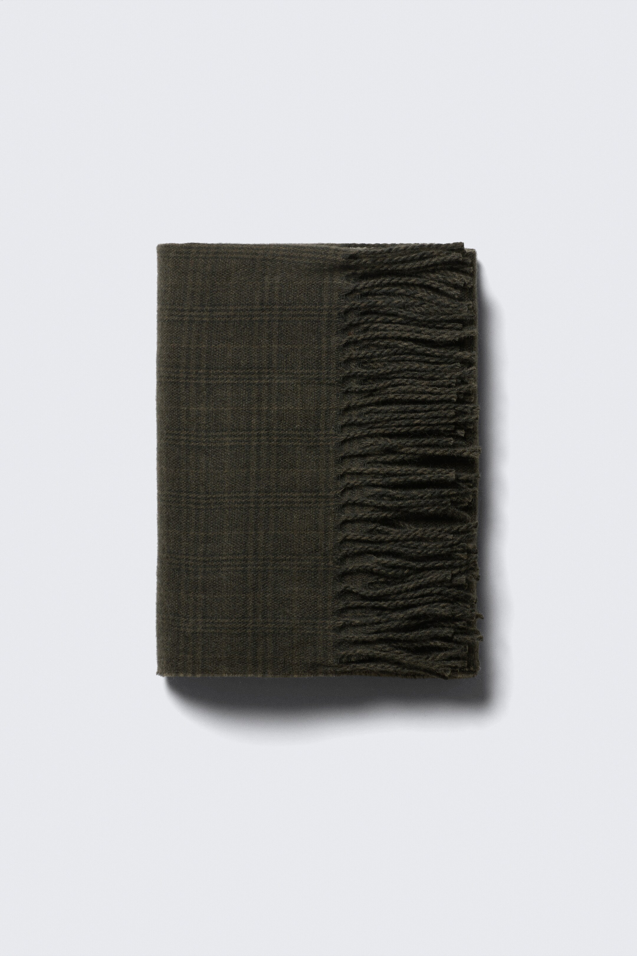 Ver imagen más grande: Una bufanda de color verde oliva oscuro está doblada en forma rectangular, revelando un sutil patrón de cuadros y flecos en un extremo.
