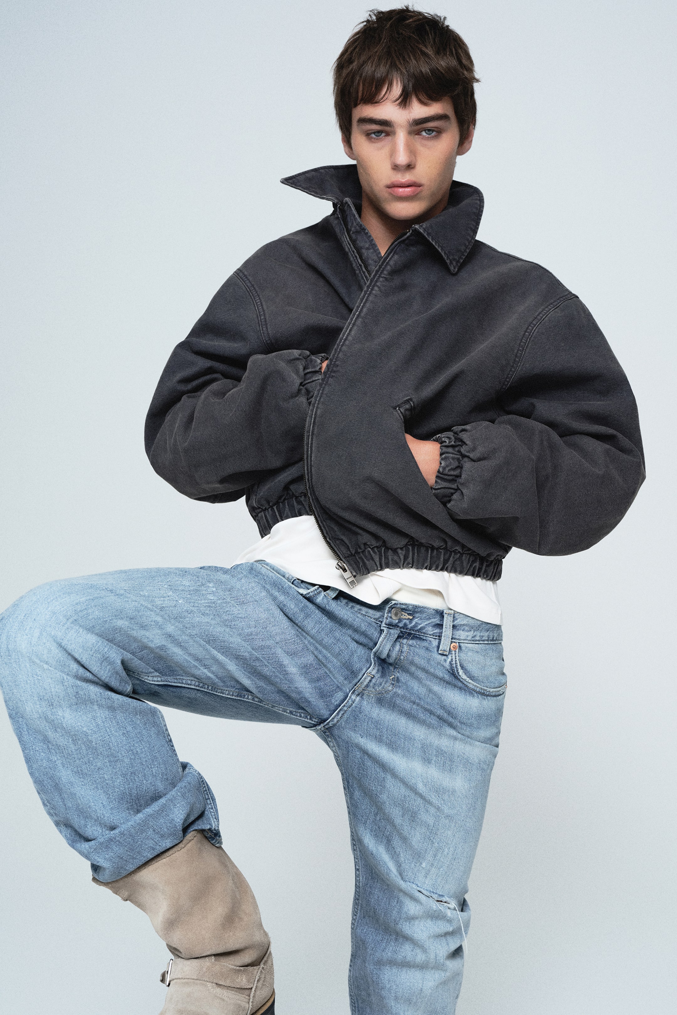 Größeres Bild ansehen: Diese Übergangsjacke in verwaschenem Schwarz ist von vorne zu sehen und präsentiert sich in einer oversized, verkürzten Passform mit überschnittenen Schultern und voluminösen Ärmeln mit elastischen Bündchen. Die Jacke verfügt über einen spitzen Kragen, einen elastischen Saum und Leistentaschen und ist über einem weißen T-Shirt getragen.
