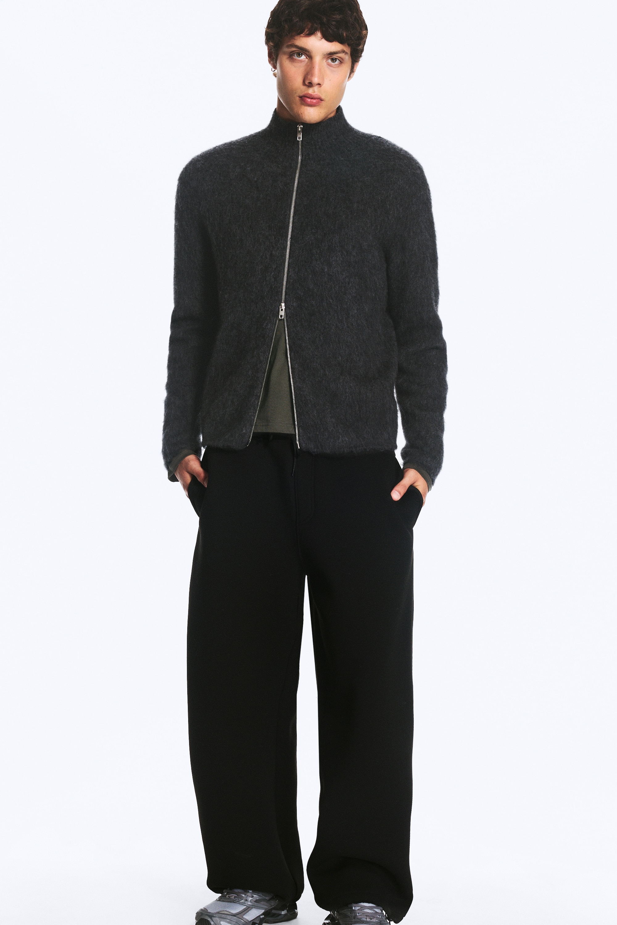 I pantaloni neri a gamba larga sono mostrati frontalmente, con una vita elasticizzata dotata di coulisse annodata. I pantaloni presentano una silhouette rilassata a gamba larga e sono rifiniti con coulisse regolabili su ciascun orlo della caviglia.