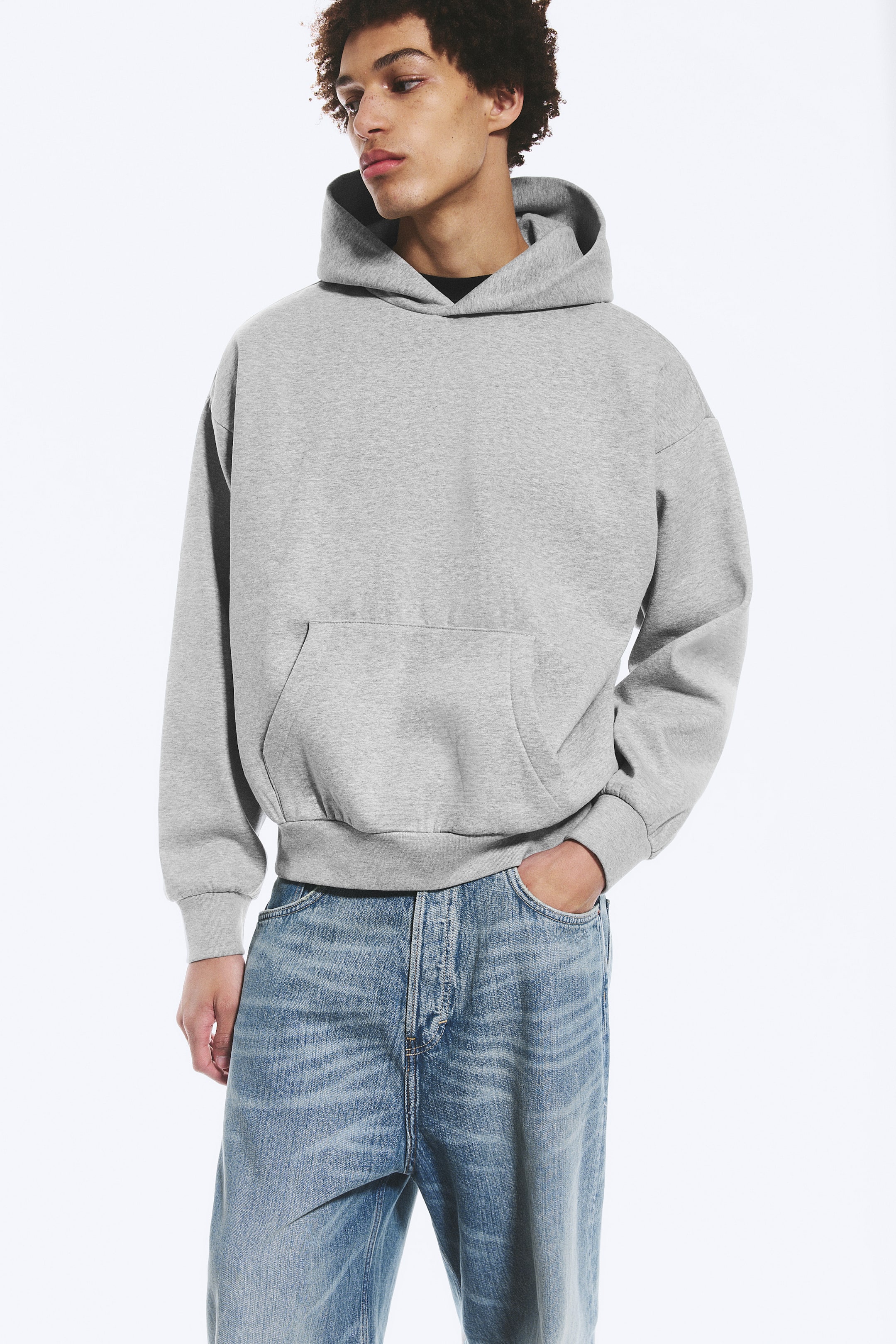 Größeres Bild ansehen: Ein grauer Kapuzenpullover wird präsentiert, der mit einer übergroßen Passform, einer strukturierten Kapuze und einer großen Kängurutasche auf der Vorderseite ausgestattet ist. Er ist mit gerippten Bündchen an den langen Ärmeln und einem gerippten Saum versehen.