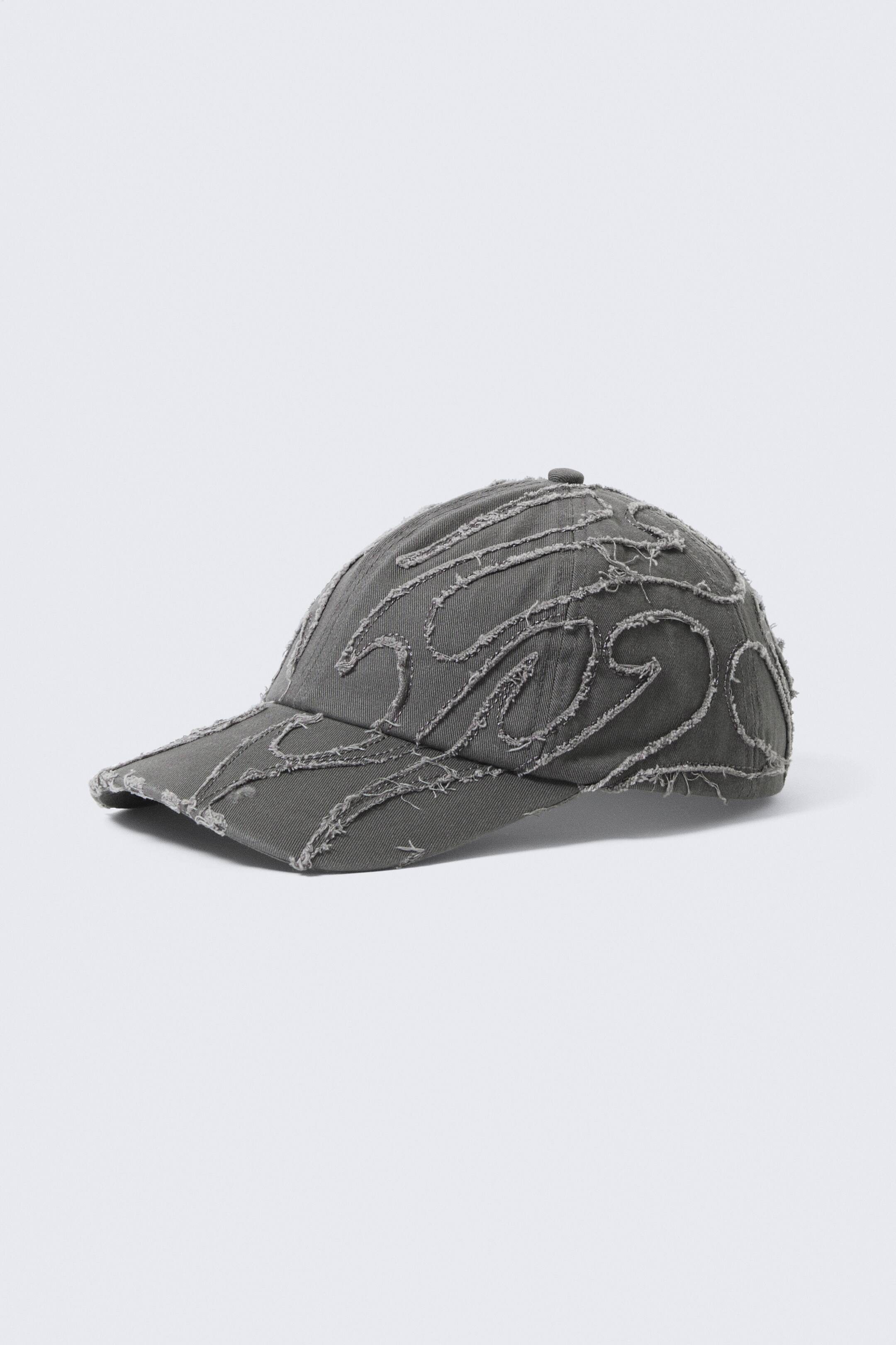 View larger image: A cotton canvas baseball cap is presented FRONT, featuring a distressed finish with frayed cut-out patterns resembling waves across its six-panel crown. It showcases a soft, unstructured shape and a pre-curved brim.