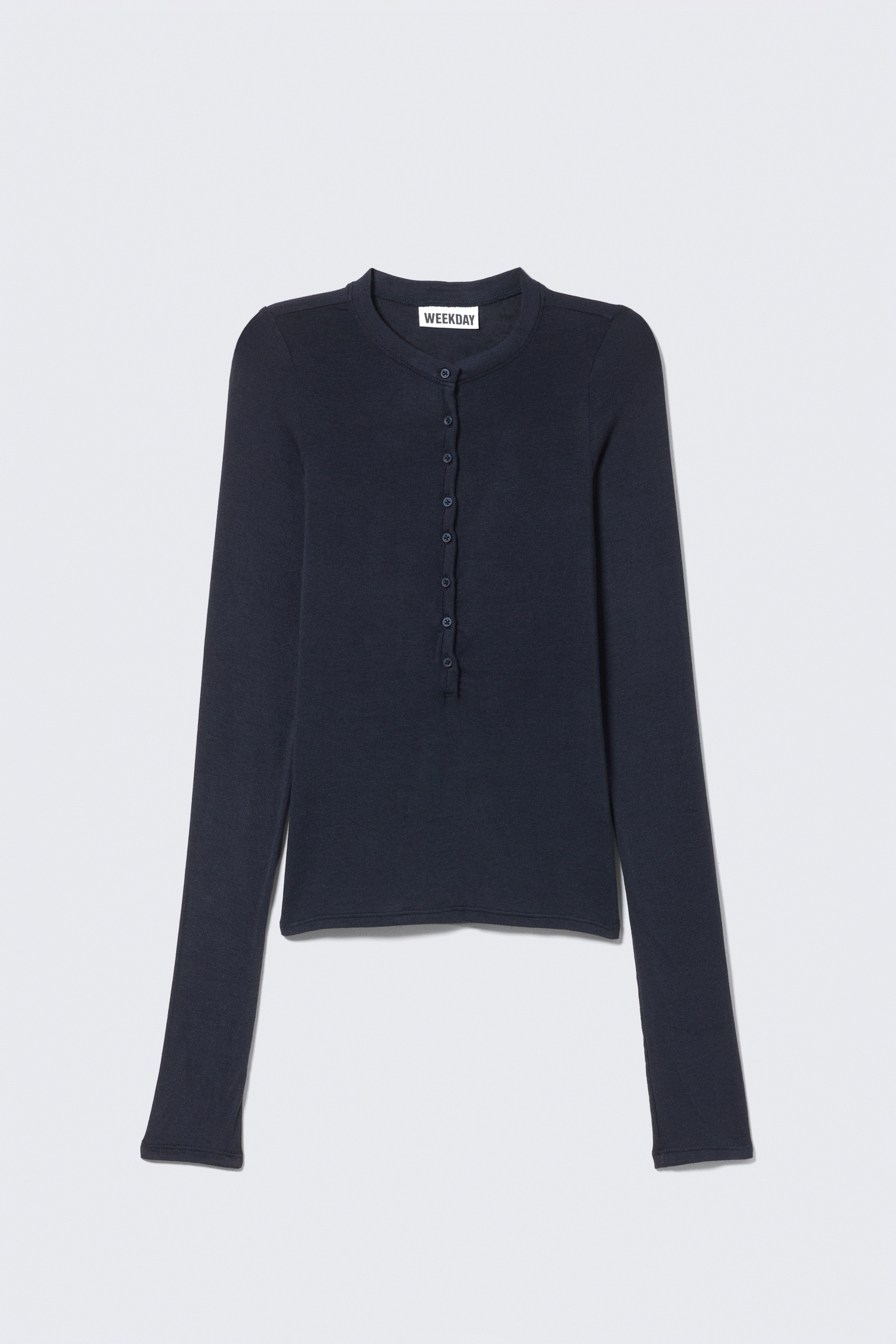 Ver imagen más grande: Un top Henley de manga larga azul oscuro se presenta como FRONT, mostrando un ajuste ceñido y una textura de jersey suave. Está caracterizado por un escote redondo con una hilera de ocho botones, mangas ligeramente más largas y dobladillos rectos.