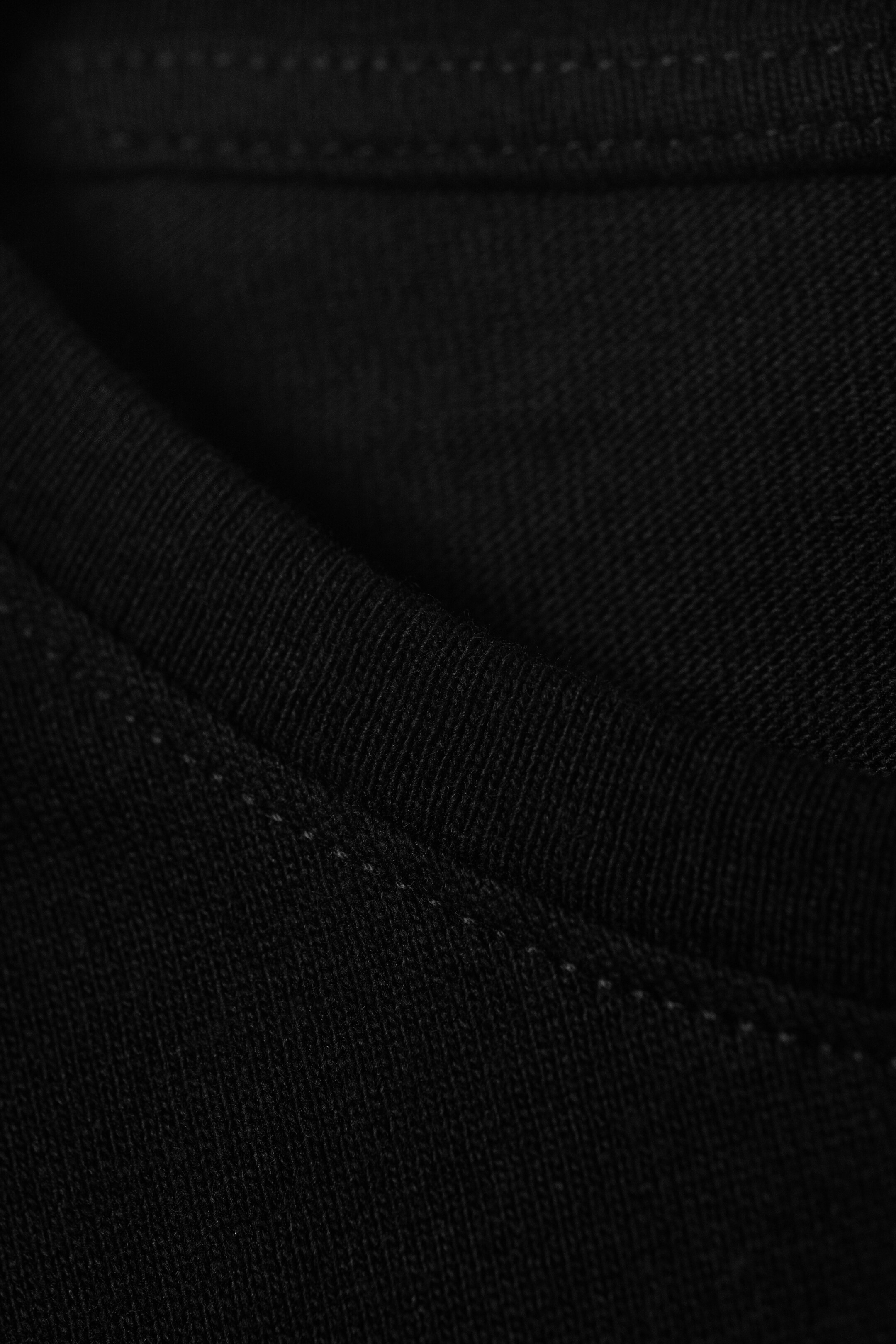 Ingrandisci l'immagine: Un indumento in maglia nera mostra la sua texture di tessuto morbido con pieghe sottili. Una doppia fila di cuciture superiori di colore chiaro corre lungo una cucitura visibile.