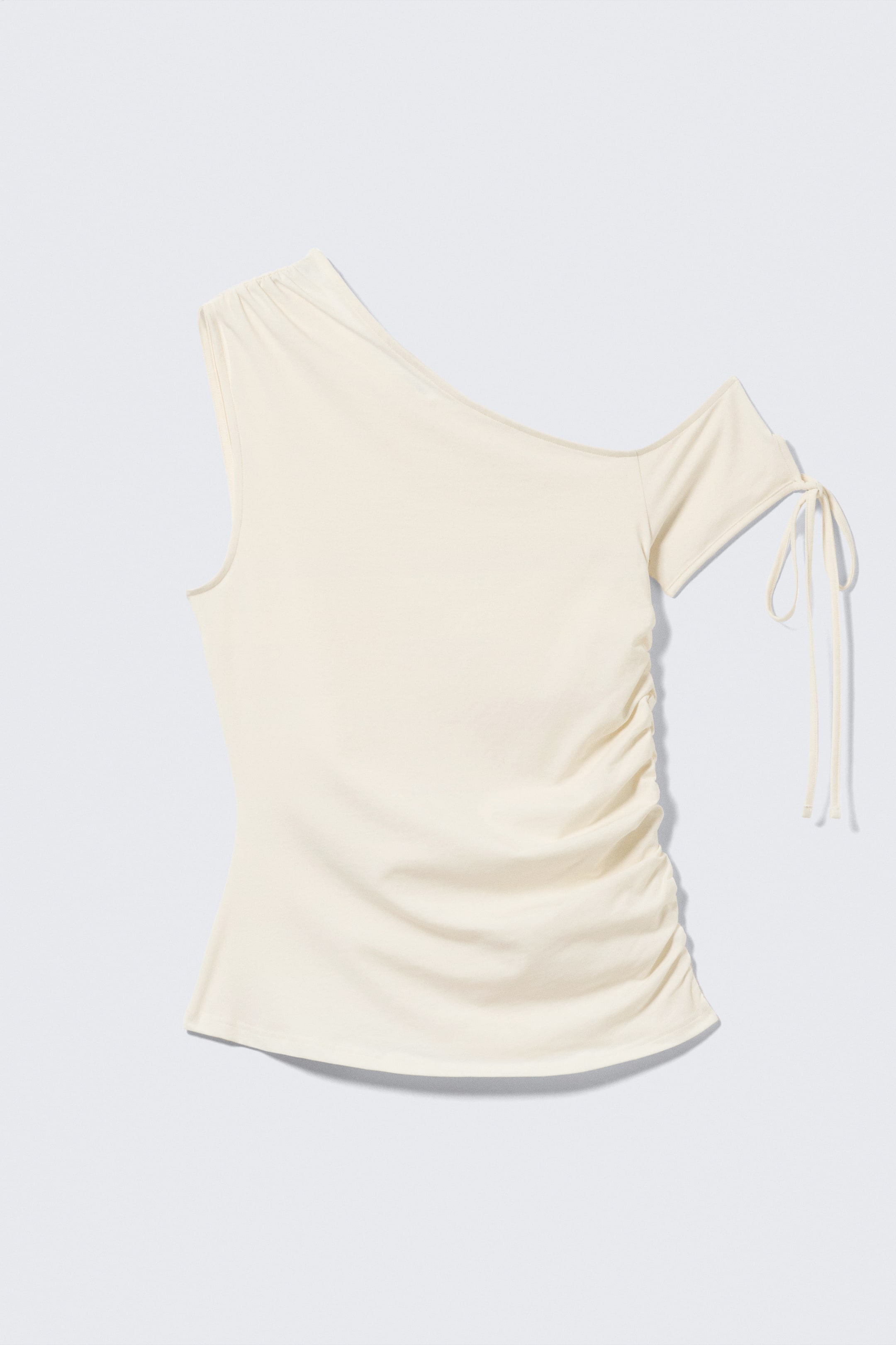Ver imagen más grande: Top crema de un solo hombro con un hombro izquierdo fruncido y una manga corta en el lado derecho, que termina con detalles de lazo. El cuerpo presenta fruncidos verticales a lo largo del lado derecho, y la prenda finaliza con un dobladillo curvado.