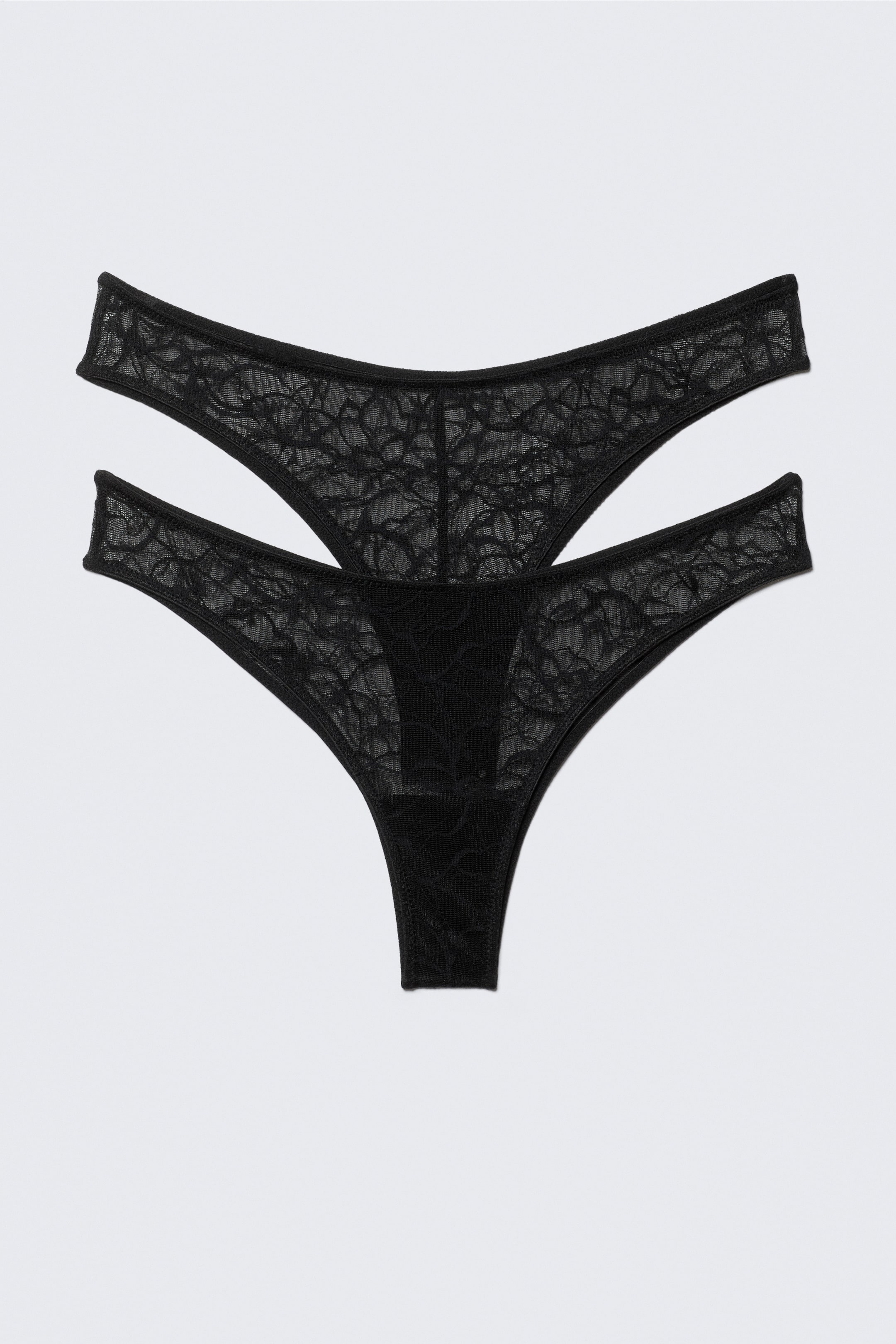 Agrandir l'image: Deux strings en dentelle noire sont posés à plat, chacun arborant un motif floral complexe sur leur tissu transparent avec des bords finis.