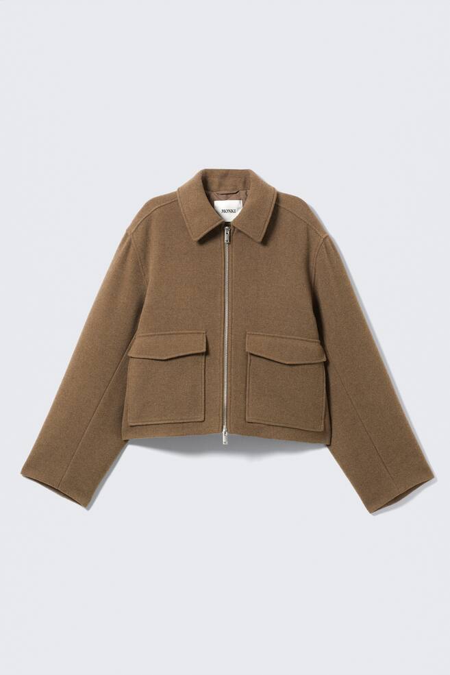 A brown cropped jacket is presented from the front, featuring a classic pointed collar, a full-length silver-tone zipper, two large flap pockets, and a relaxed, boxy fit. - 1