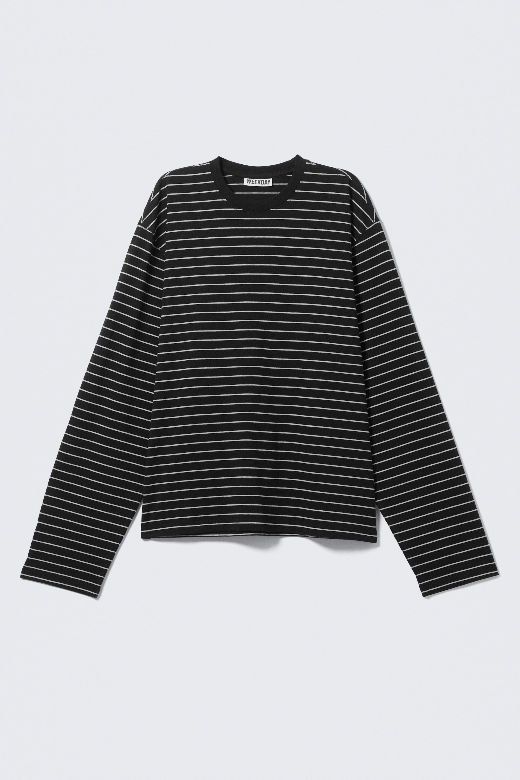 Grösseres Bild ansehen: Ein langärmliges T-Shirt wird von VORNE gezeigt, mit einer lockeren, kastigen Passform, einem runden, gerippten Ausschnitt und einem geraden Saum. Das Shirt ist mit dünnen weißen horizontalen Streifen auf schwarzem Hintergrund gemustert, und ein "WEEKDAY"-Label ist im inneren hinteren Ausschnitt sichtbar.
