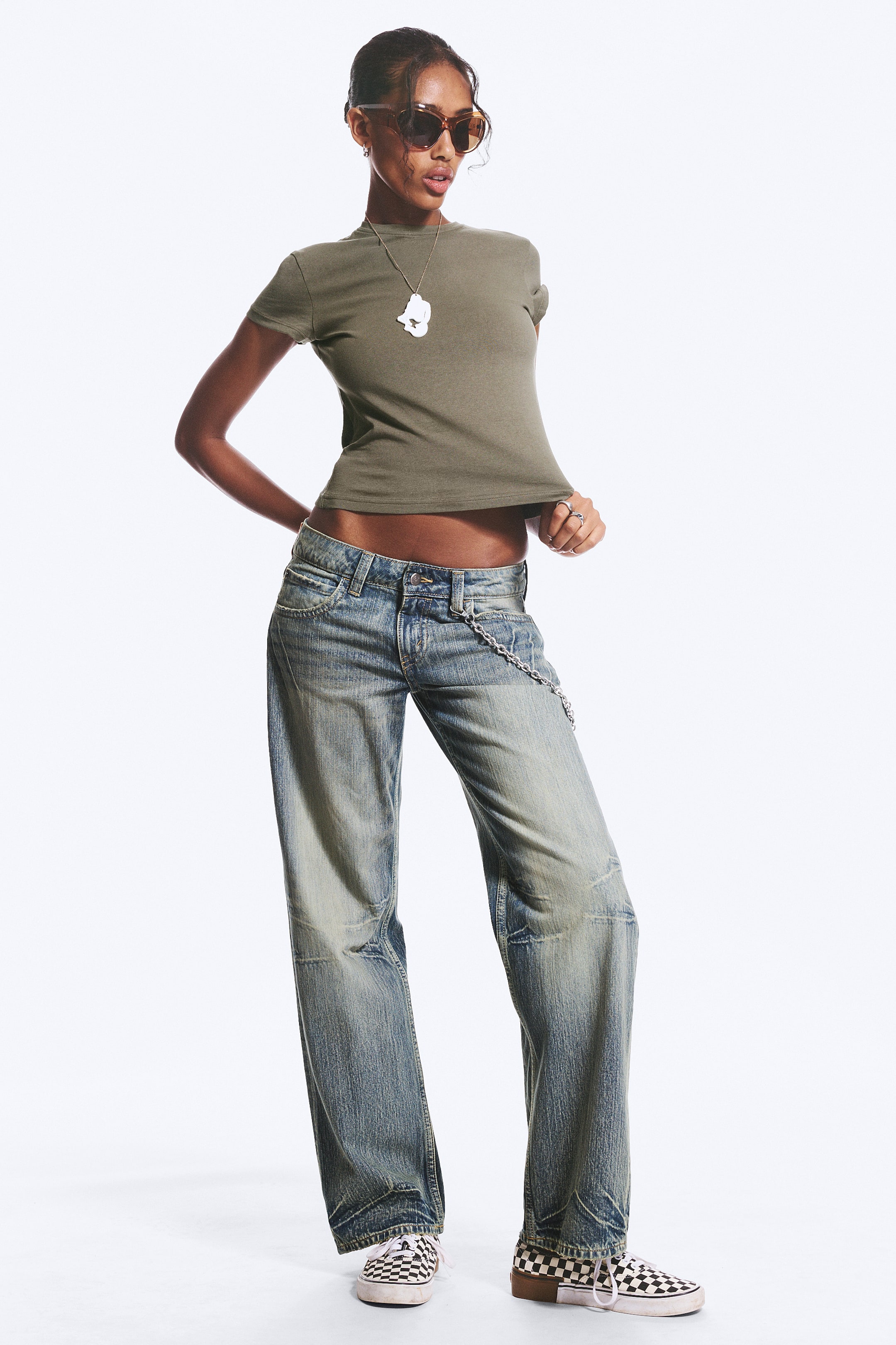 Visa större bild: Ett par jeans med en blekt blå denimtvätt och en baggy, vida ben och låg midja. Jeansen har slitna fläckar och mörkare slitna områden på låren och knäna, och en silverfärgad kedja hänger från en främre bältesögla.