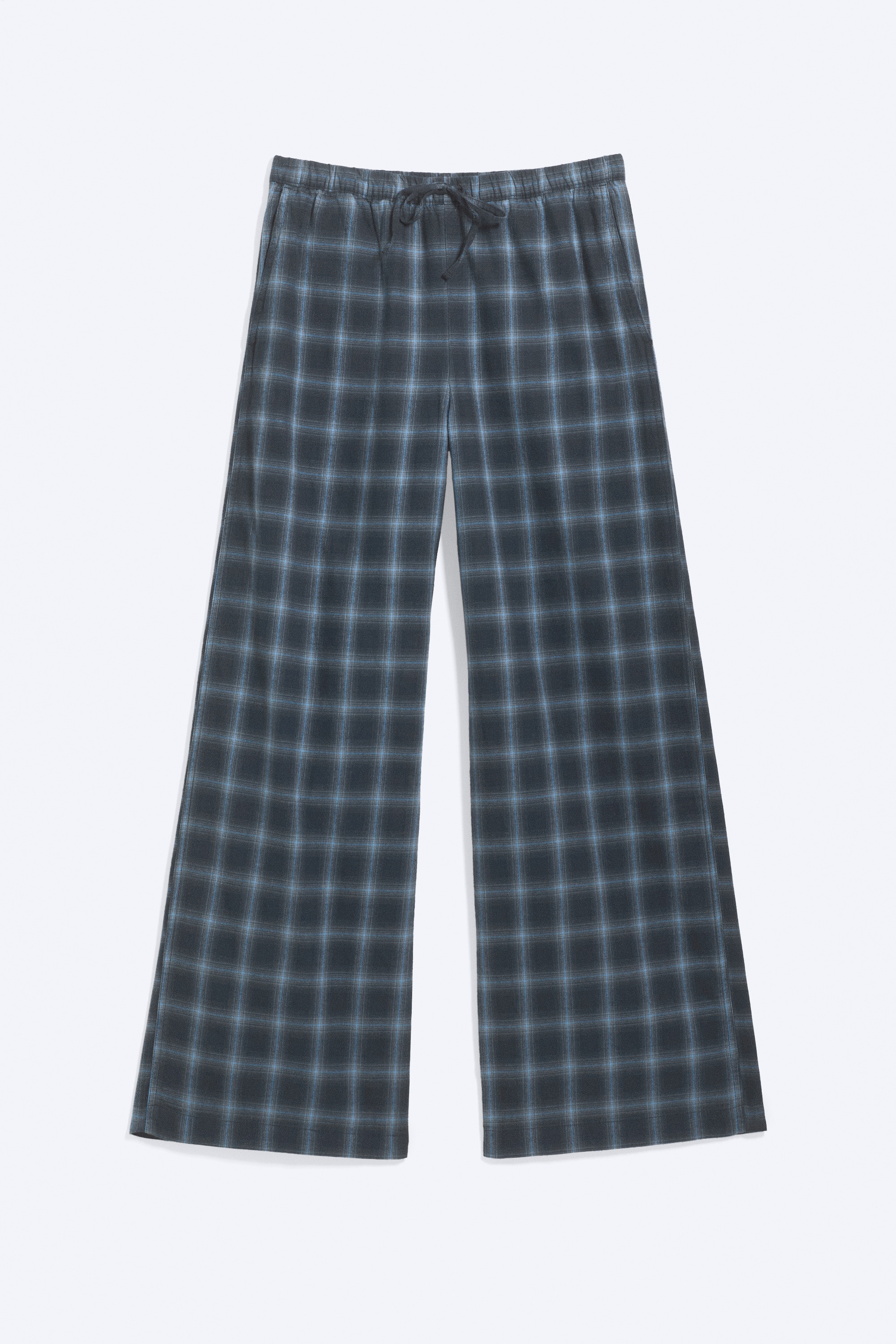 Pantaloni da pigiama in flanella a gamba ampia con motivo a quadri blu, indossati dalla modella in profilo laterale. I pantaloni presentano una vita elasticizzata a media altezza con coulisse e sono abbinati a un top a maniche lunghe grigio scuro.