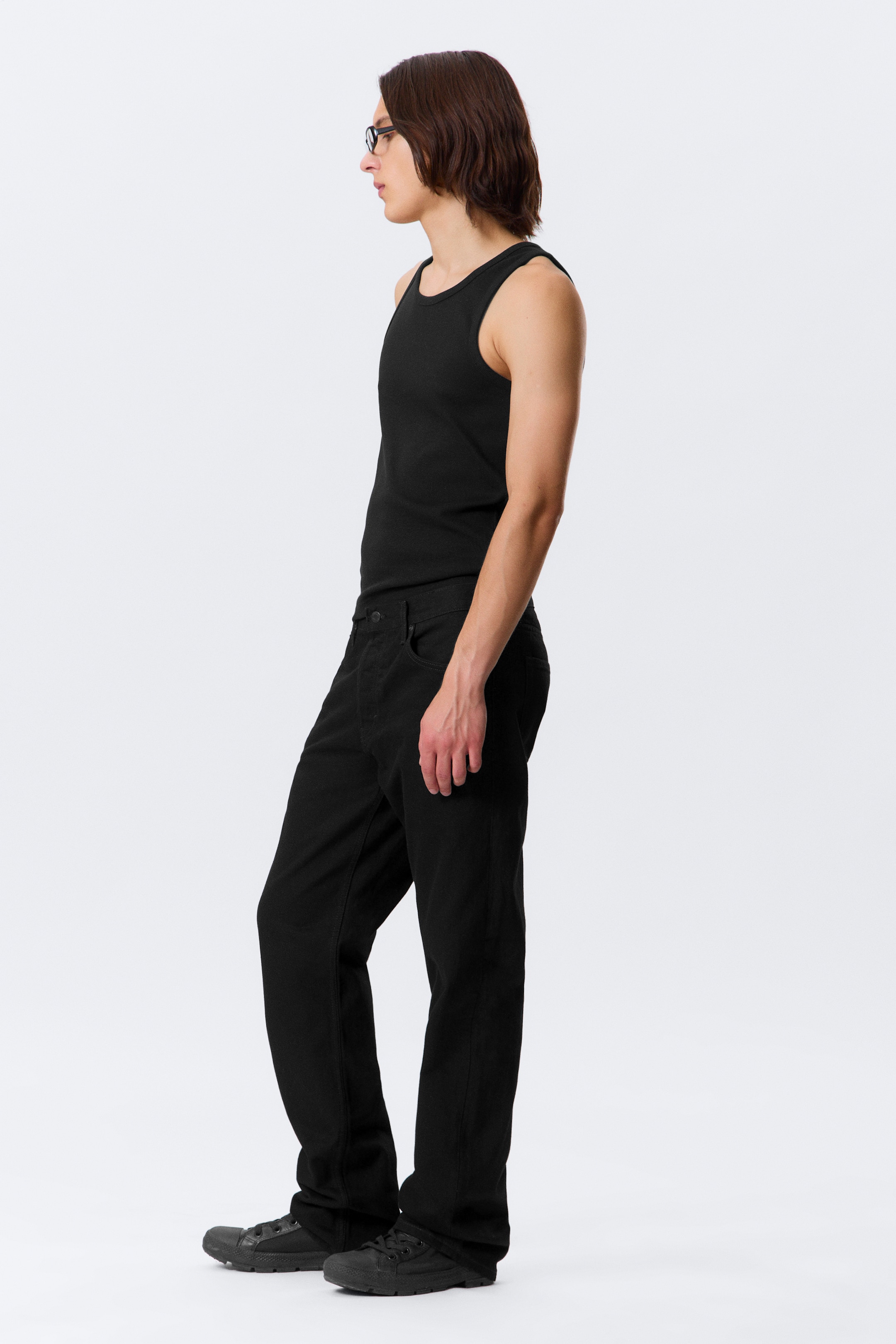 View larger image: A black ribbed tank top is being worn, fitting closely to the torso and featuring a rounded neckline, shown from a side view. Black relaxed-fit pants are also being worn, falling straight and pooling slightly over black low-top sneakers.