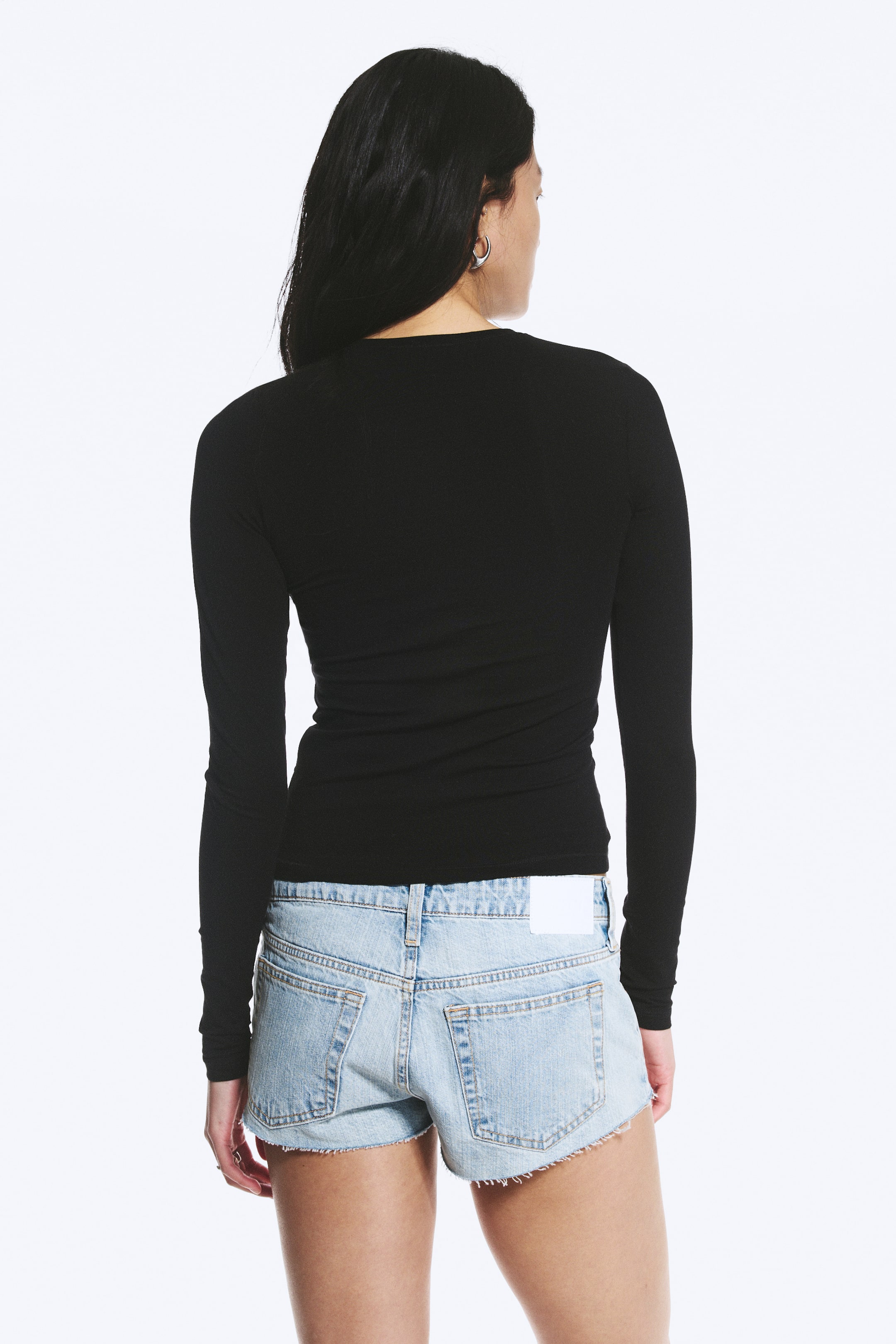Visualizza l'immagine ingrandita: Un top nero a maniche lunghe viene presentato dal retro, caratterizzato da una silhouette aderente e uno scollo rotondo.