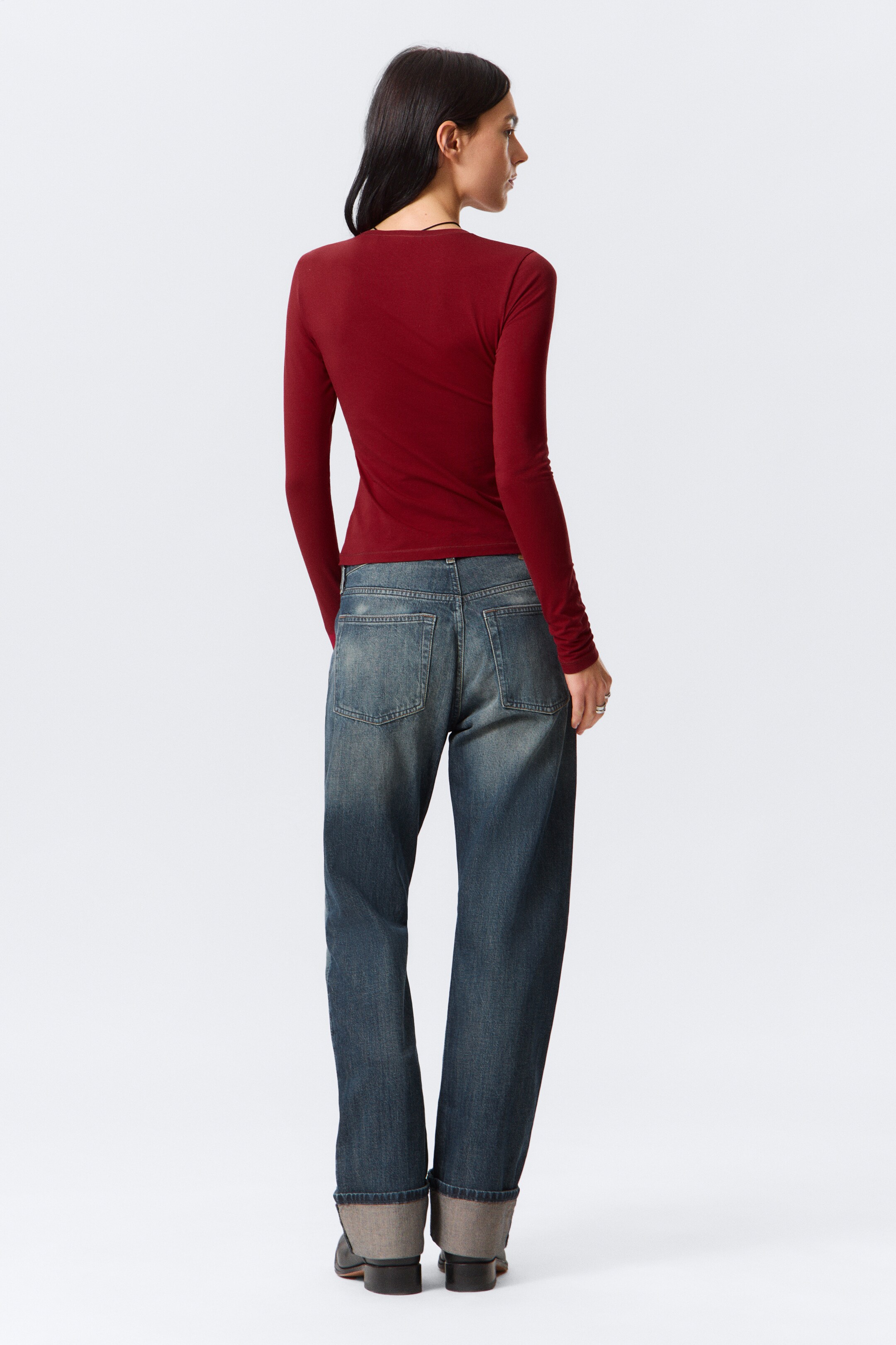 Grotere afbeelding bekijken: Een paar donkerblauwe denim jeans wordt van de achterkant getoond, met een ontspannen, rechte pijp. Ze hebben een vervaagde wassing met twee zichtbare achterzakken en brede omgeslagen zomen, die het lichtere interieur van de denim onthullen.