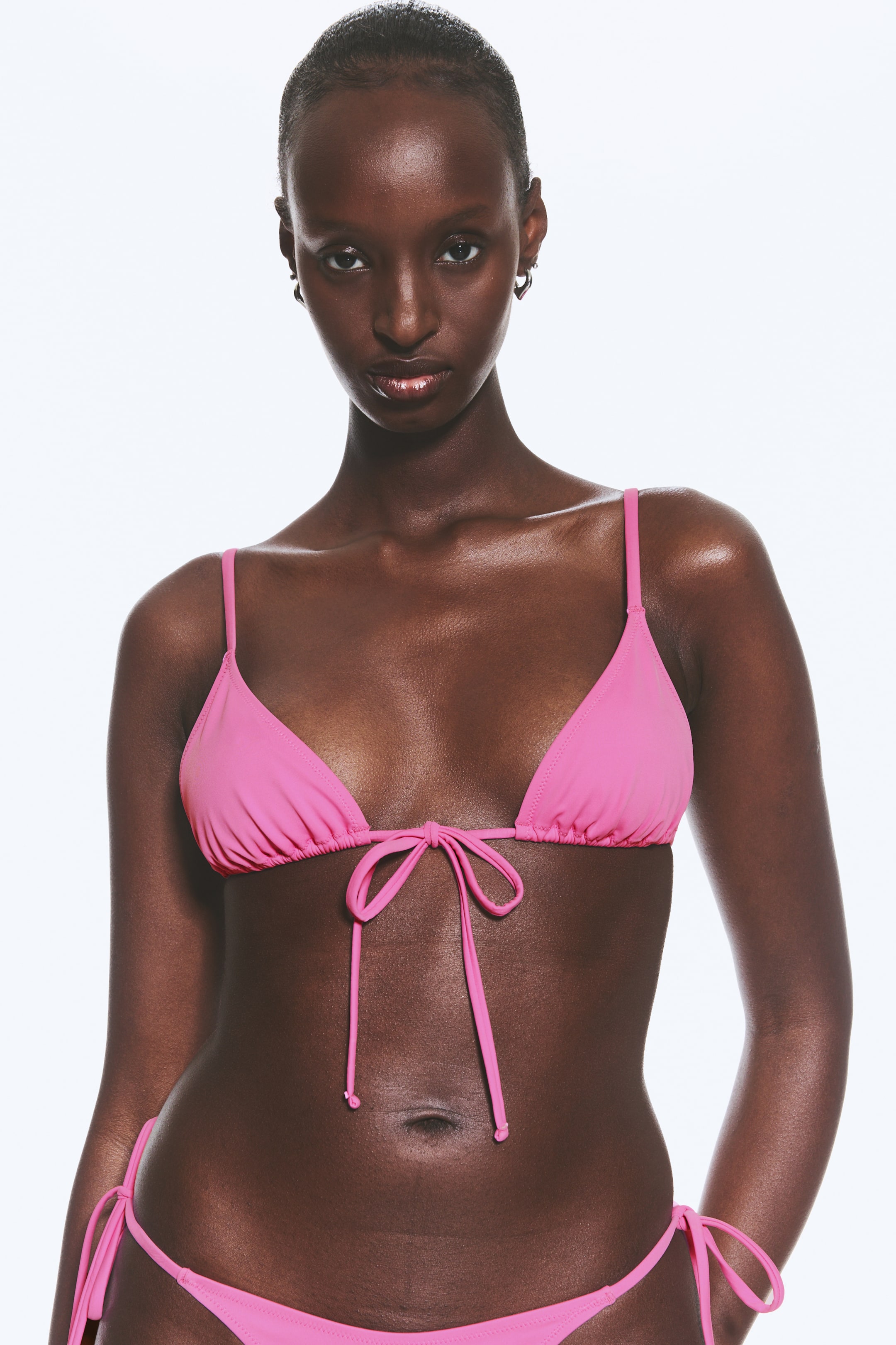 View larger image: A pink bikini featuring a triangle top with thin shoulder straps and a central front tie fastening, paired with matching tie-side bikini bottoms.