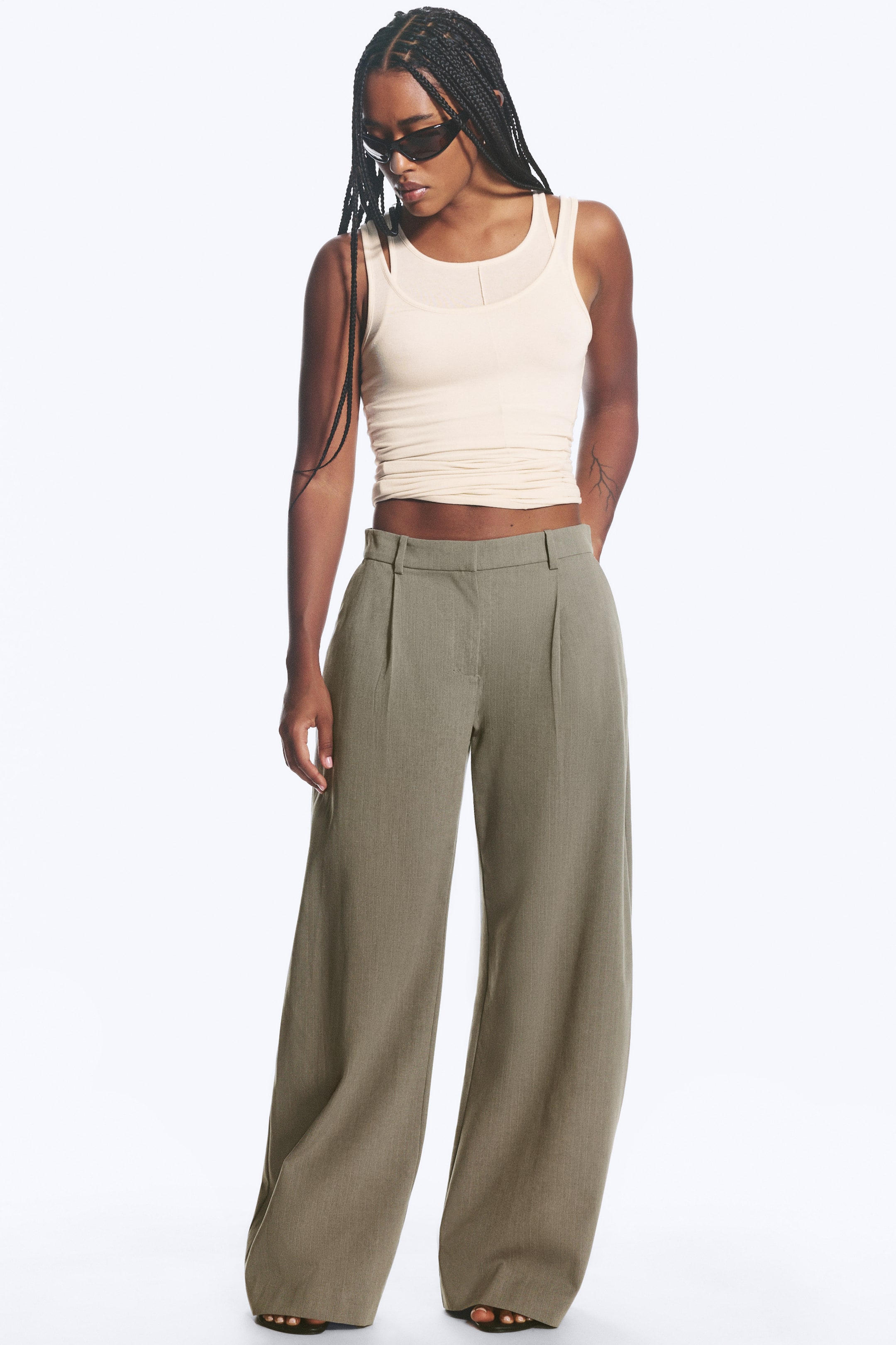 Agrandir l'image: Le mannequin porte un pantalon de costume taille basse vert olive, avec des jambes larges, des plis marqués à l'avant et des poches latérales en biais.