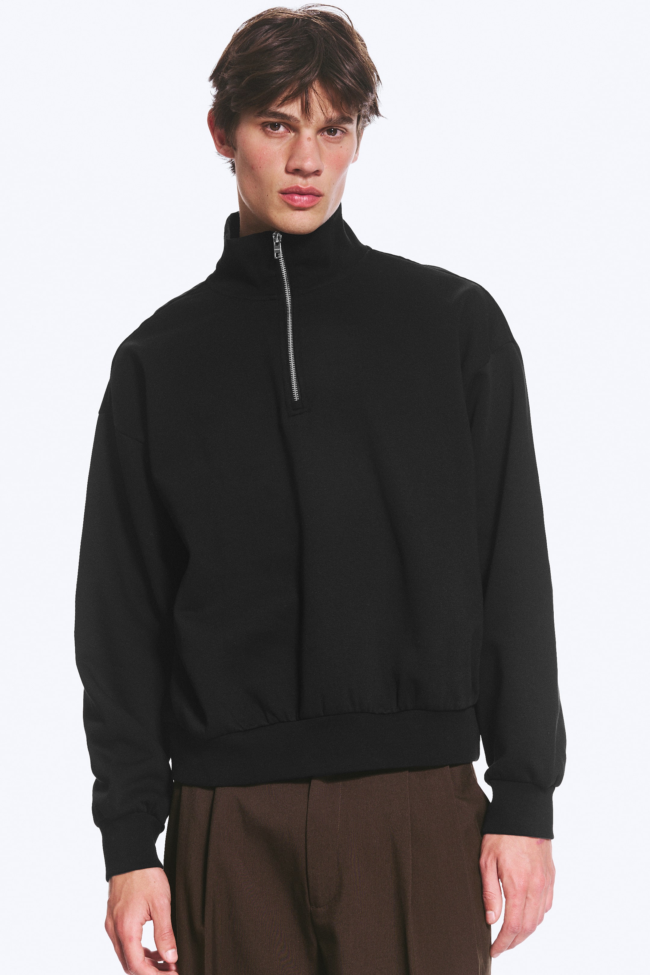 Ver imagen más grande: Se presenta una sudadera negra con cremallera de un cuarto desde el frente, que cuenta con un cuello alto con cremallera plateada, un ajuste holgado y puños y dobladillo acanalados.