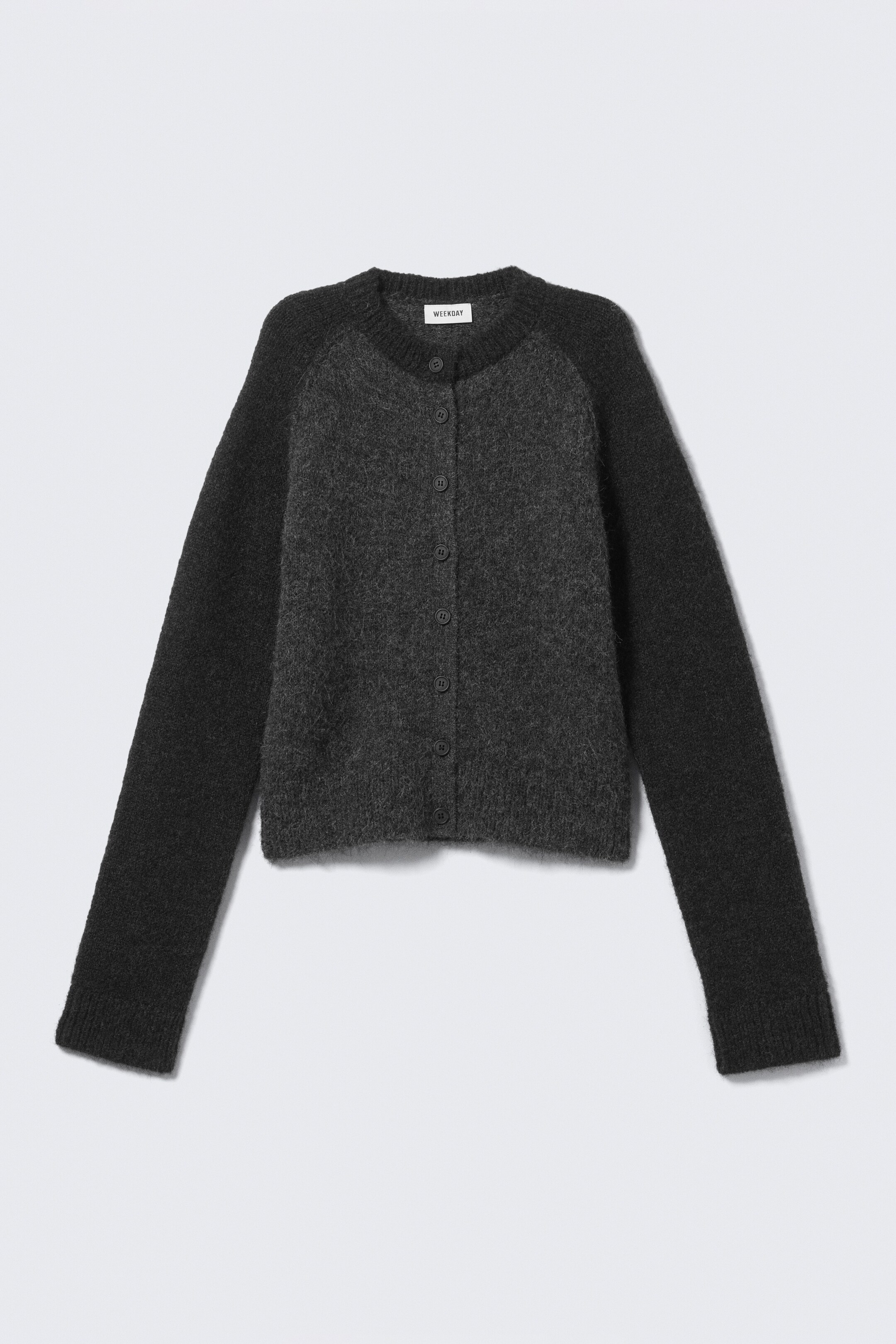 Visualizza immagine più grande: Un cardigan bicolore è mostrato dalla parte anteriore, con un corpo grigio scuro e maniche raglan grigio più scuro. Il cardigan presenta una texture morbida, un collo rotondo con l'etichetta del marchio "WEEKDAY" e una chiusura frontale completa con sette bottoni scuri, oltre a polsini e orlo a coste.
