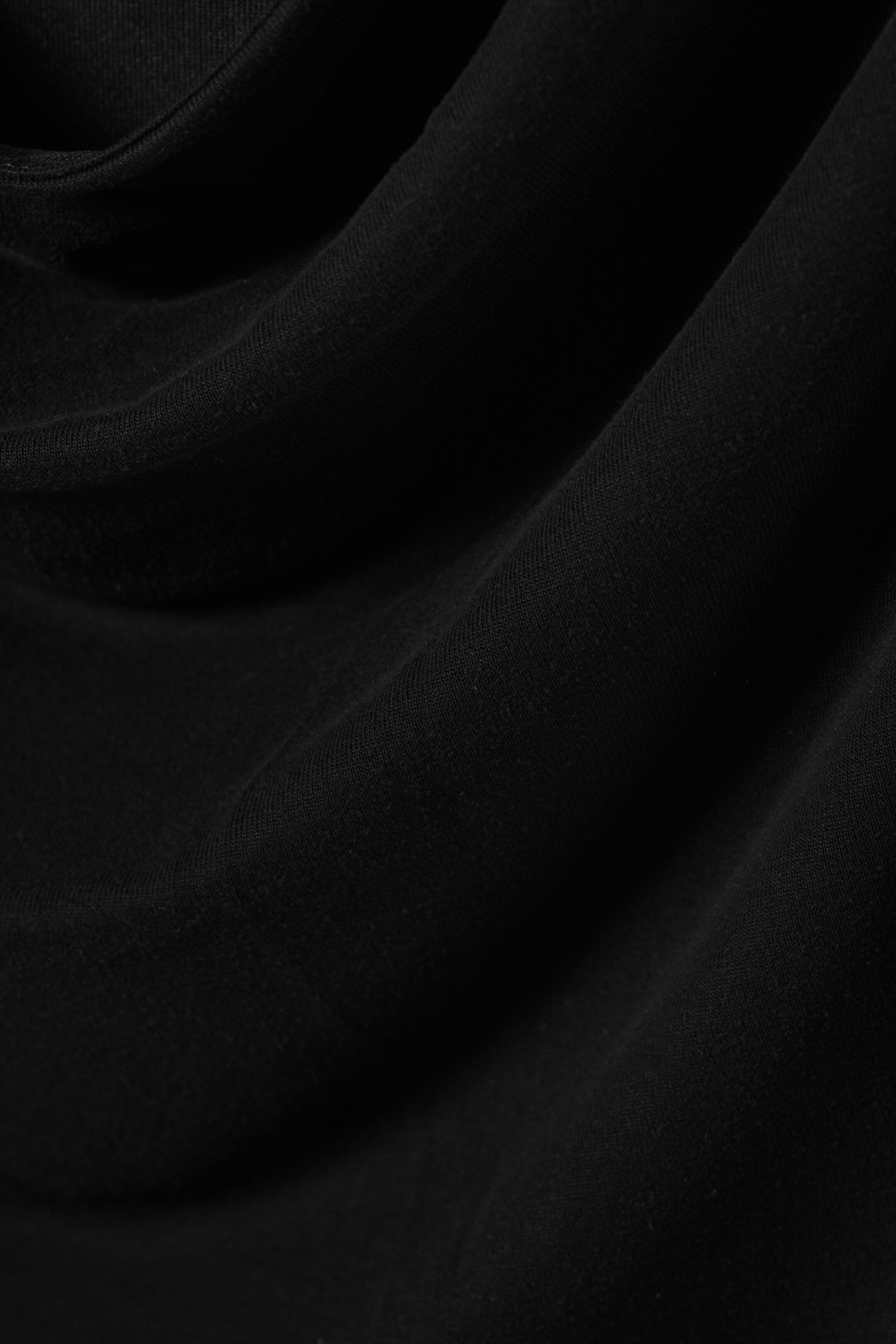 Visa större bild: Svart tyg draperar och viker sig, vilket skapar mjuka kurvor och skuggor som framhäver dess subtilt texturerade yta.