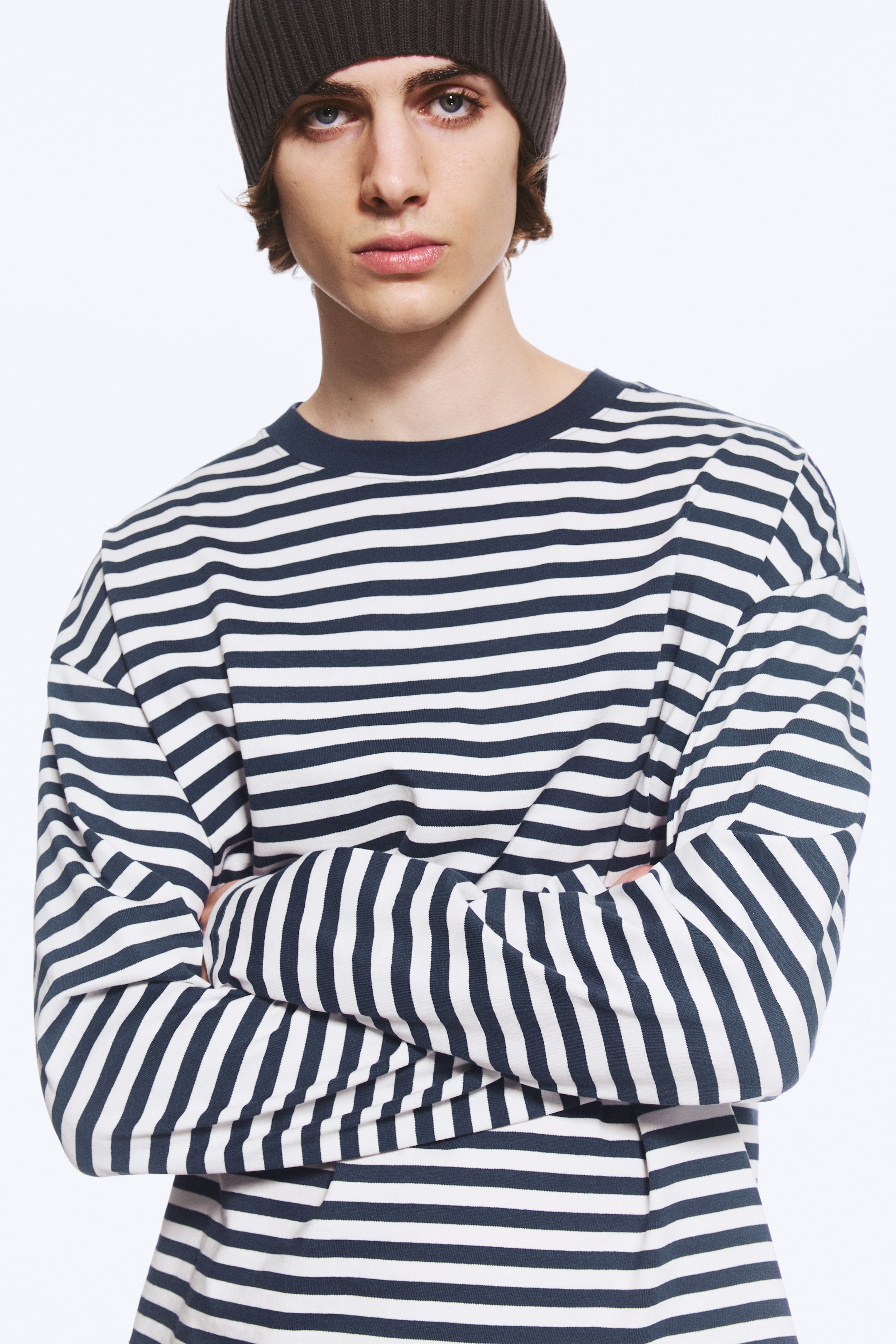Se større billede: En boxy T-shirt med lange ærmer, horisontale striber i marineblå og hvid samt en ensfarvet marineblå rund hals bæres af modellen, som står med armene over kors.