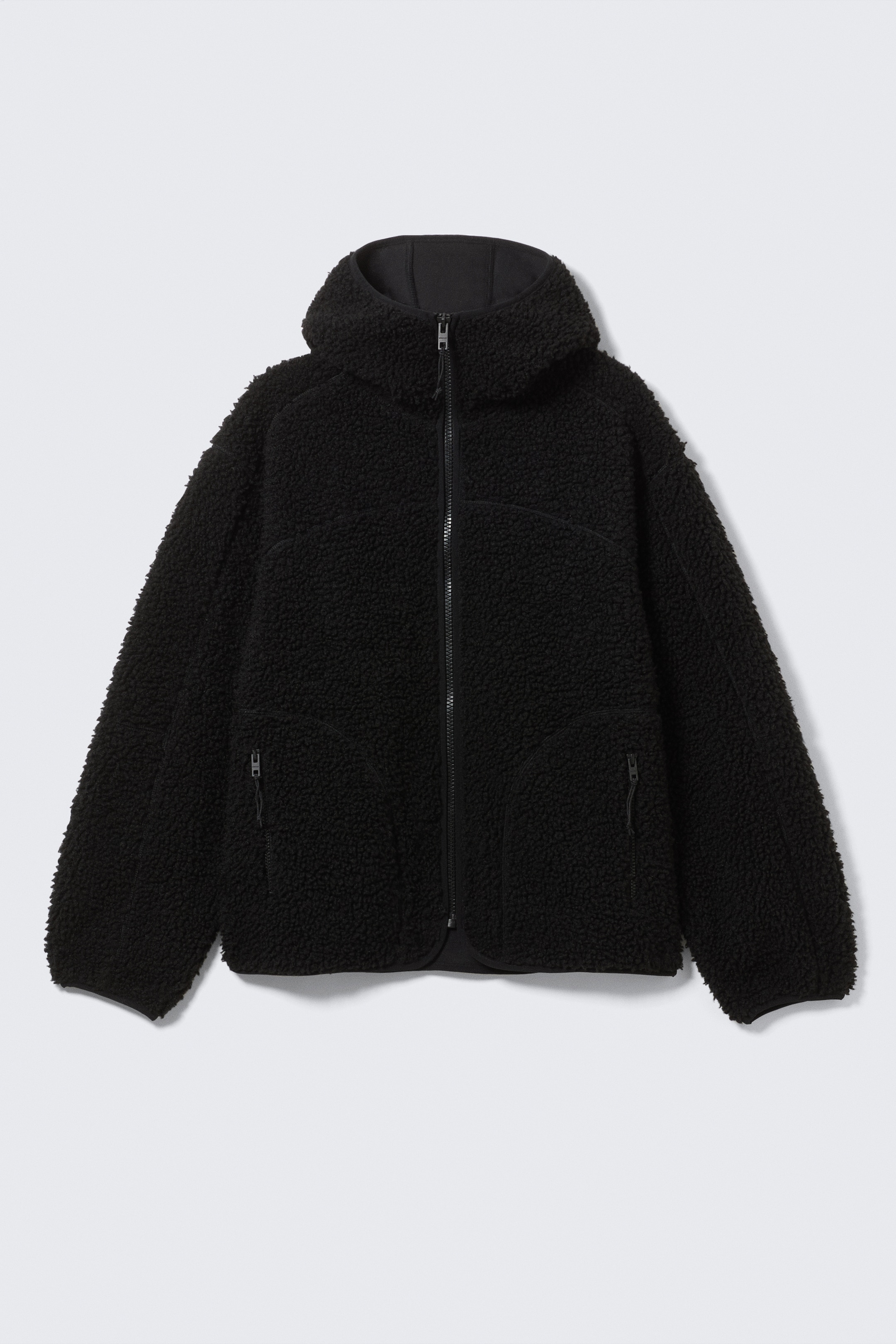 Visualizza immagine più grande: Una giacca in pile sherpa nero presenta una chiusura frontale con cerniera completa, un cappuccio con fodera interna liscia nera, due tasche laterali con cerniera e linee di cucitura curve che dettagliano la parte anteriore.