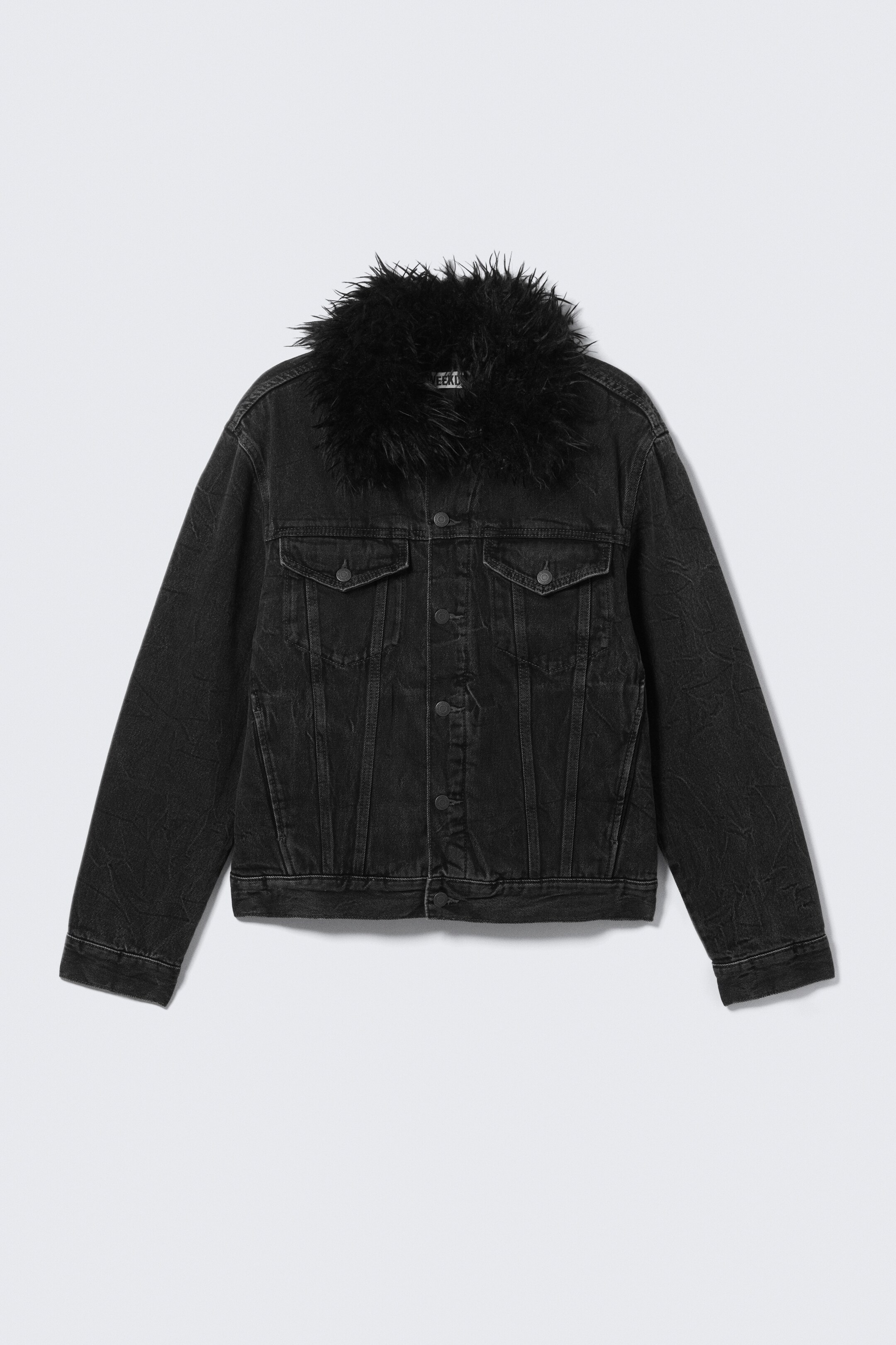View larger image: A black denim jacket is presenting FRONT, featuring a shaggy black faux fur collar. It is displaying two buttoned flap chest pockets, a front button closure, and a slightly faded, relaxed fit.