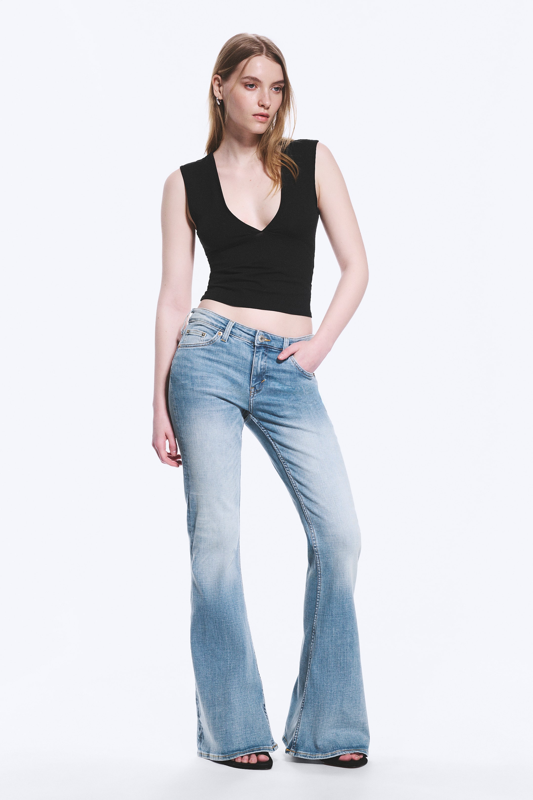 Größeres Bild ansehen: Ein Paar hellblaue Jeans mit einem ausgewaschenen Look, der sich zu den ausgestellten unteren Beinen hin verdunkelt. Die Jeans haben eine niedrige Taille, Fronttaschen und einen Knopf- und Reißverschluss, die ab dem Knie ausgestellt sind.