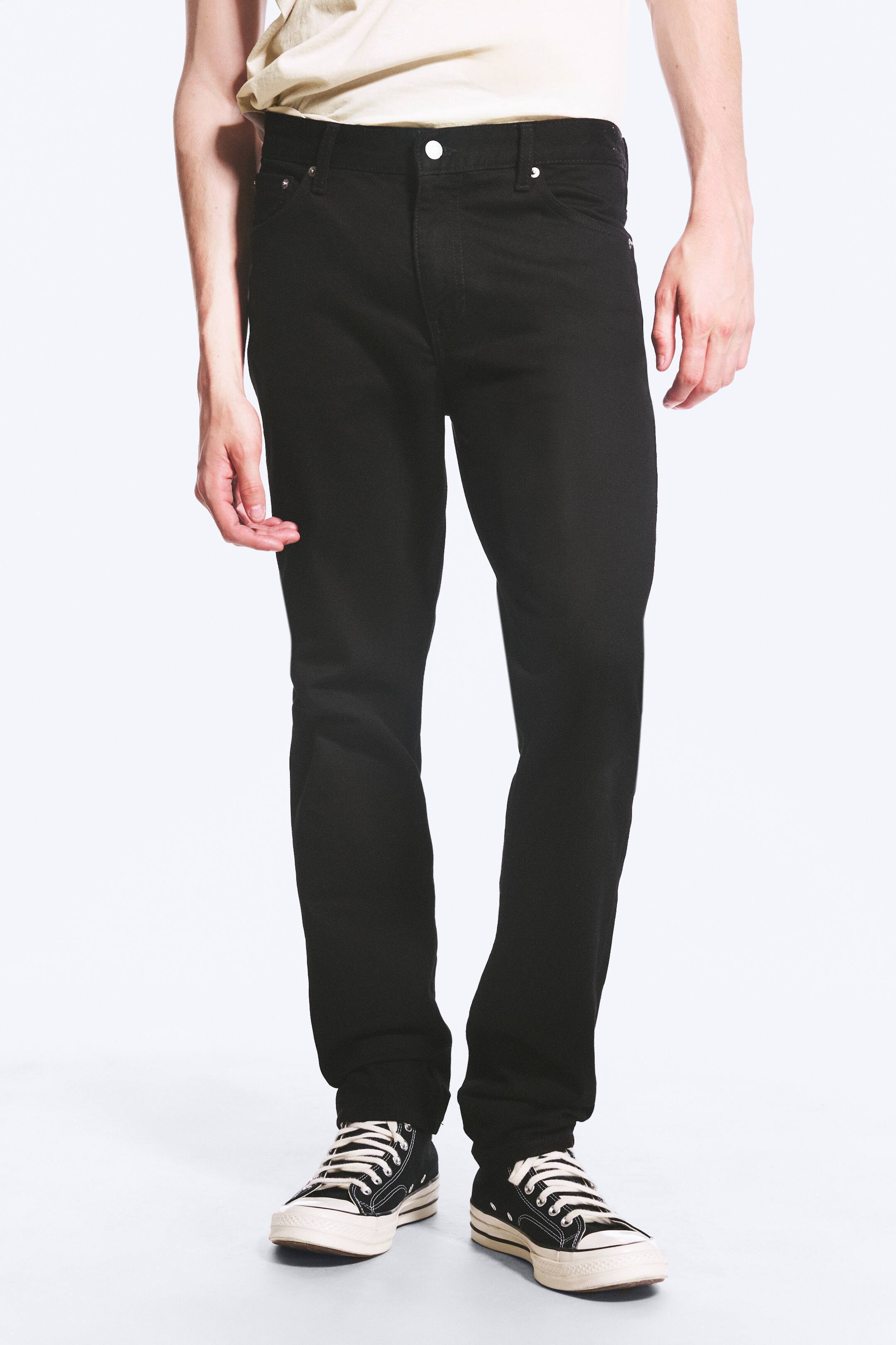 Visualizza immagine più grande: I jeans neri vengono presentati con una vestibilità dritta lungo la gamba e una chiusura frontale con bottone e zip. Le gambe dei pantaloni a lunghezza intera poggiano sulle scarpe.