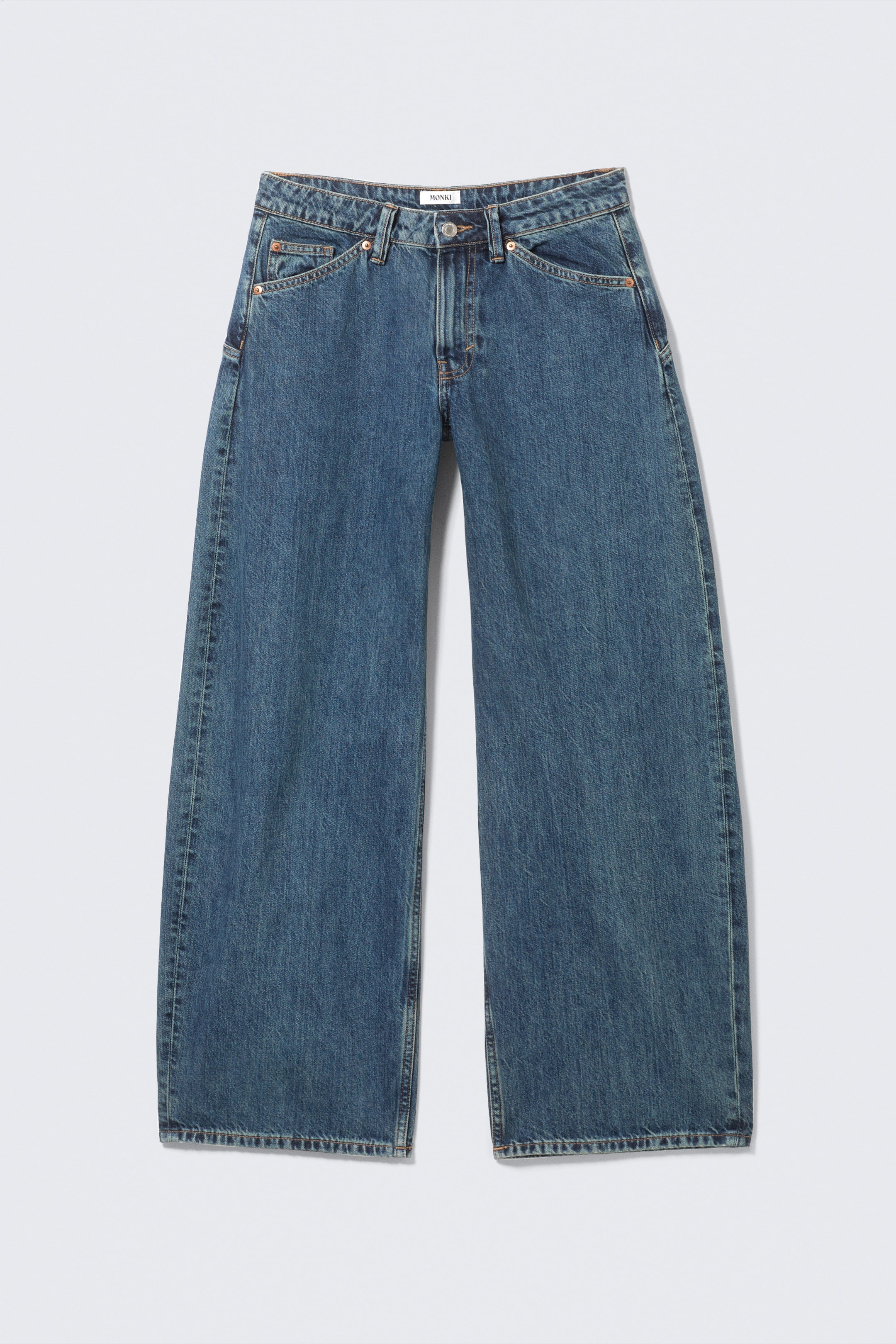 Visualizza immagine più grande: Jeans in denim blu presentano il DAVANTI, caratterizzati da una vestibilità ampia e rilassata. Sono progettati con chiusura a bottone e zip, passanti per cintura e tasche frontali angolate, inclusa una piccola tasca per monete, tutti dettagliati con cuciture a contrasto visibili. Una piccola etichetta bianca "MONKI" è visibile sulla cintura posteriore.