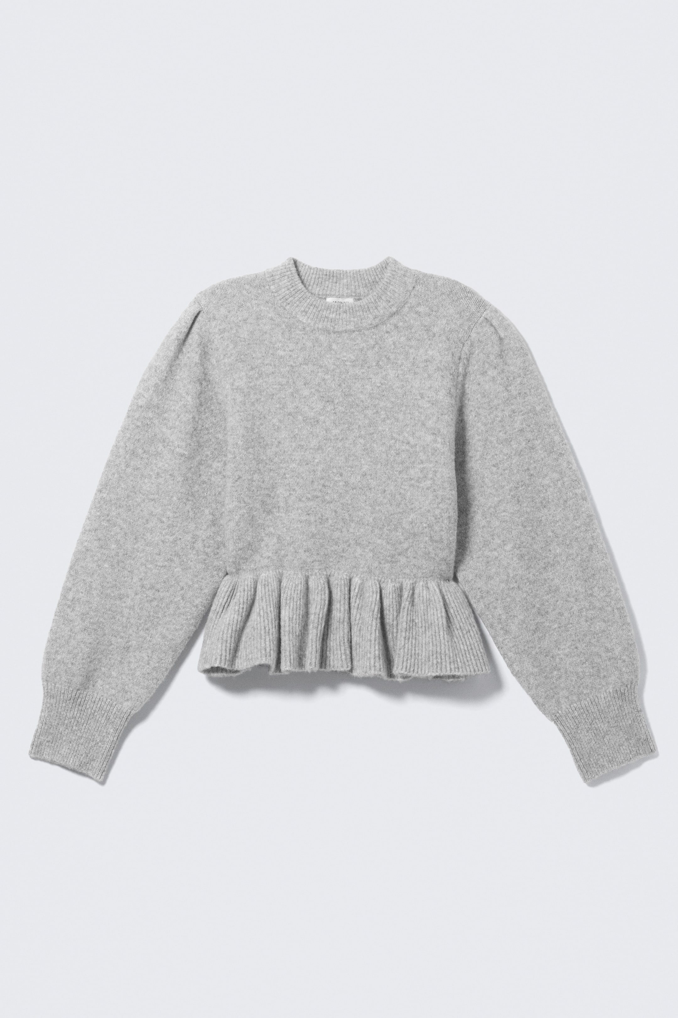 Ver imagen más grande: Un jersey gris jaspeado muestra su parte frontal, con un cuello redondo acanalado y mangas largas con un sutil detalle de abullonado en los hombros y puños acanalados. Un dobladillo peplum plisado da forma a la parte inferior del jersey.