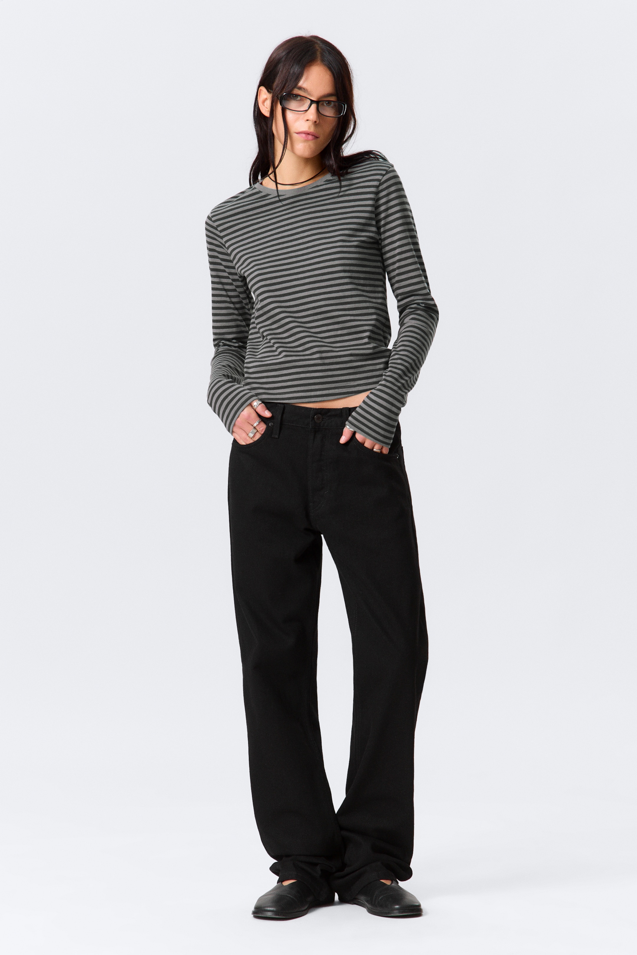 View larger image: A long-sleeved top with horizontal dark grey and medium grey stripes is being shown, featuring a cropped hem and extra-long sleeves that are gathering at the hands. It is being paired with black wide-leg jeans that are pooling at the ankles.