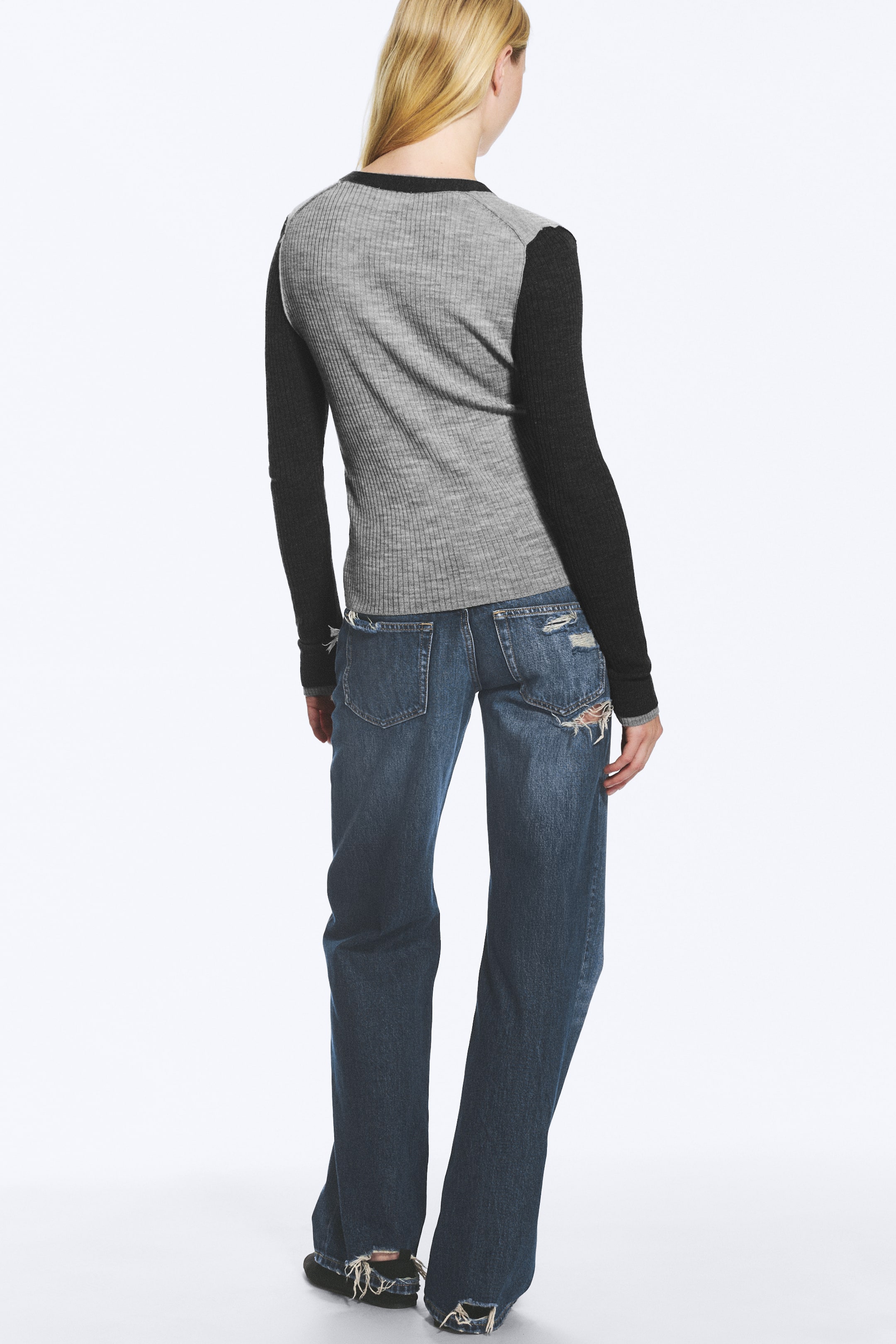 Visualizza immagine più grande: La modella indossa un top a maniche lunghe, visto da dietro. Presenta un corpo a coste grigio e maniche lunghe nere a tinta unita a contrasto, abbinato a jeans blu effetto distressed.
