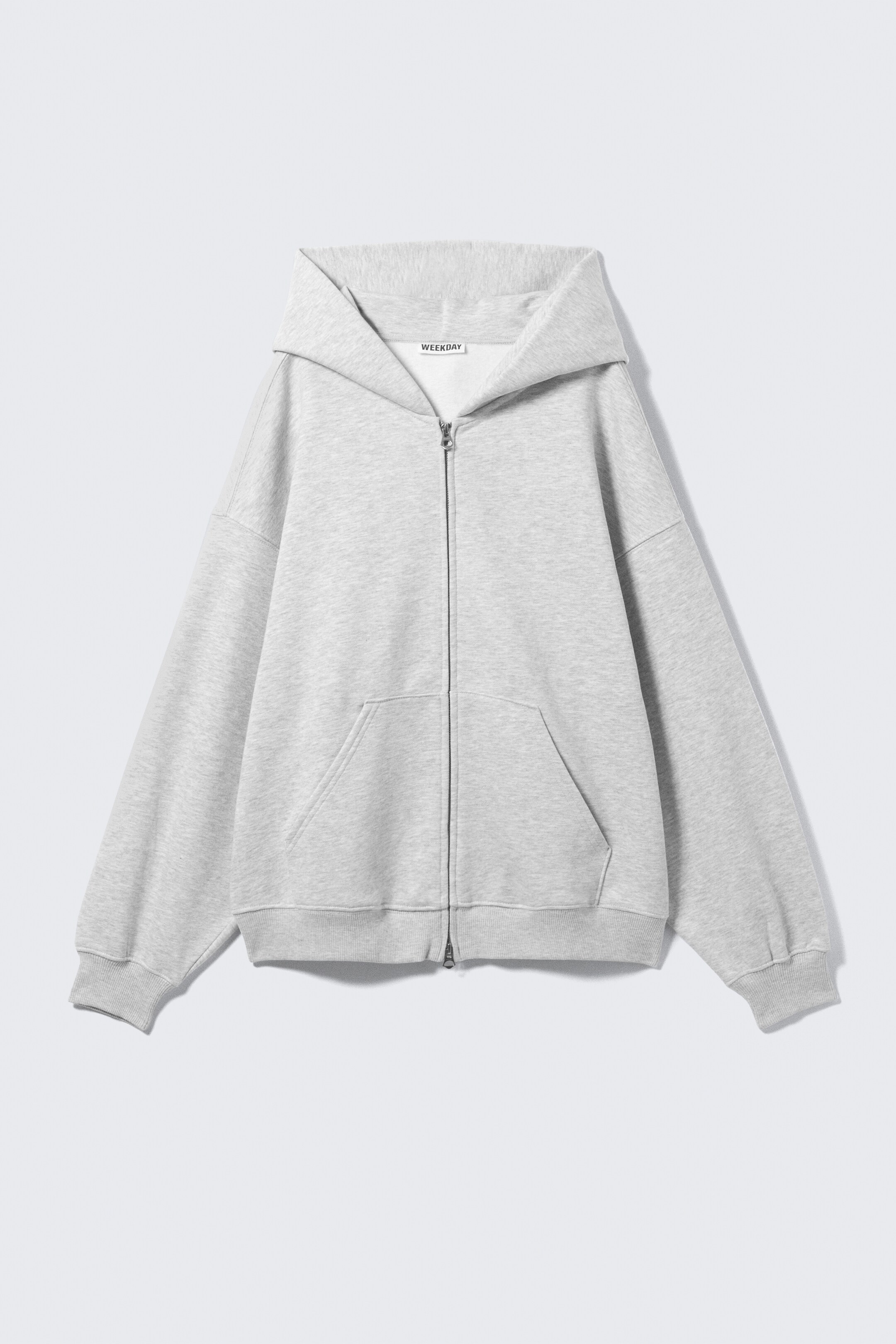 View larger image: A heavy-weight, light grey zip hoodie is displayed from the FRONT, featuring an oversized, slouchy silhouette in a soft cotton-blend fleece fabric. It includes a spacious double-layered hood without drawstrings, dropped shoulders, a visible two-way silver-toned zip, large front pockets, and ribbed cuffs and hem.