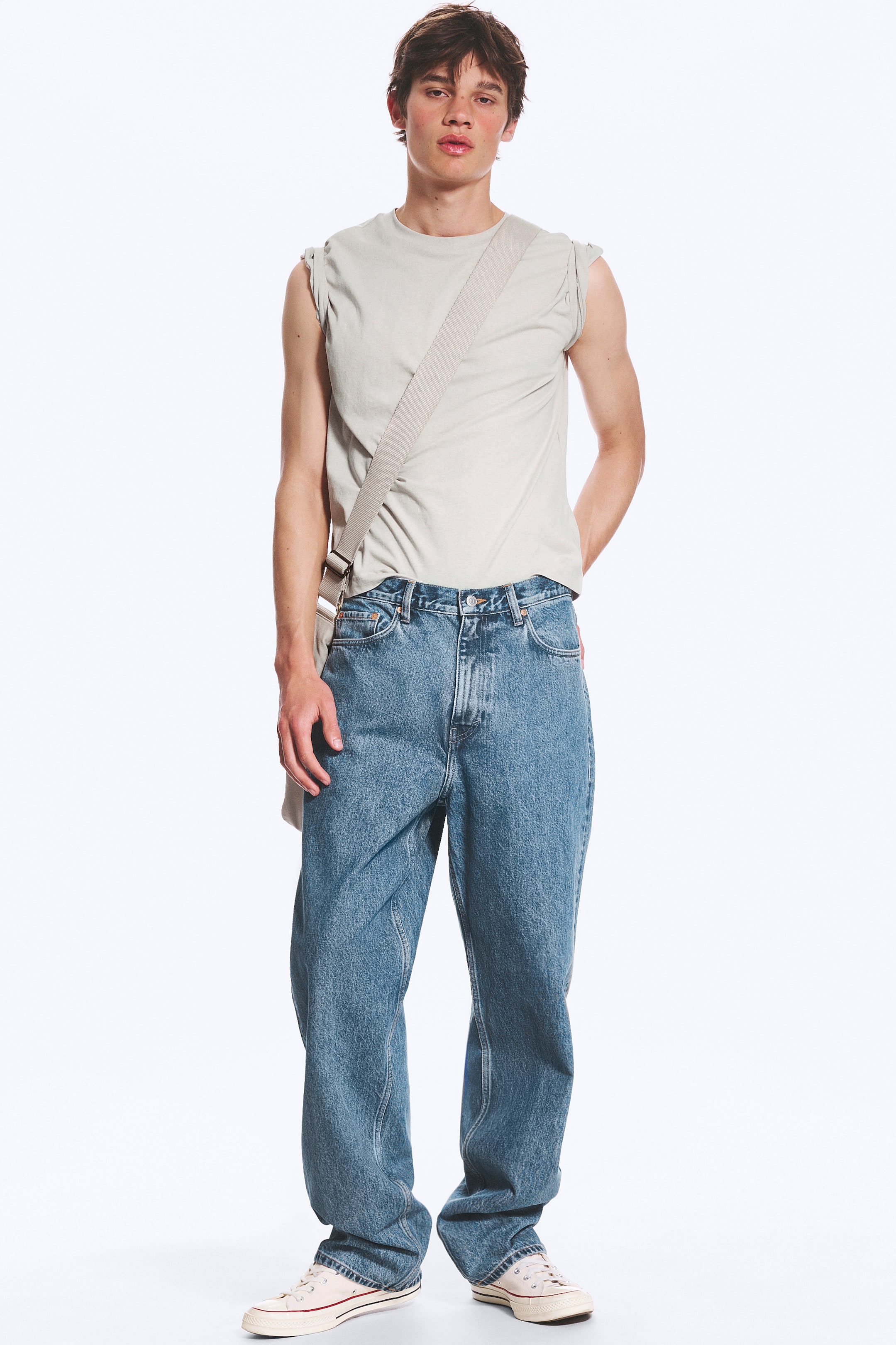 Visa större bild: Blå denimjeans med en avslappnad, rak passform och en medelblå tvätt, visade från en frontal vinkel. De är designade med hög midja och en synlig knapp- och dragkedjestängning, bärs med en ljus ärmlös topp delvis instoppad i midjebandet och faller över krämfärgade canvas-skor.