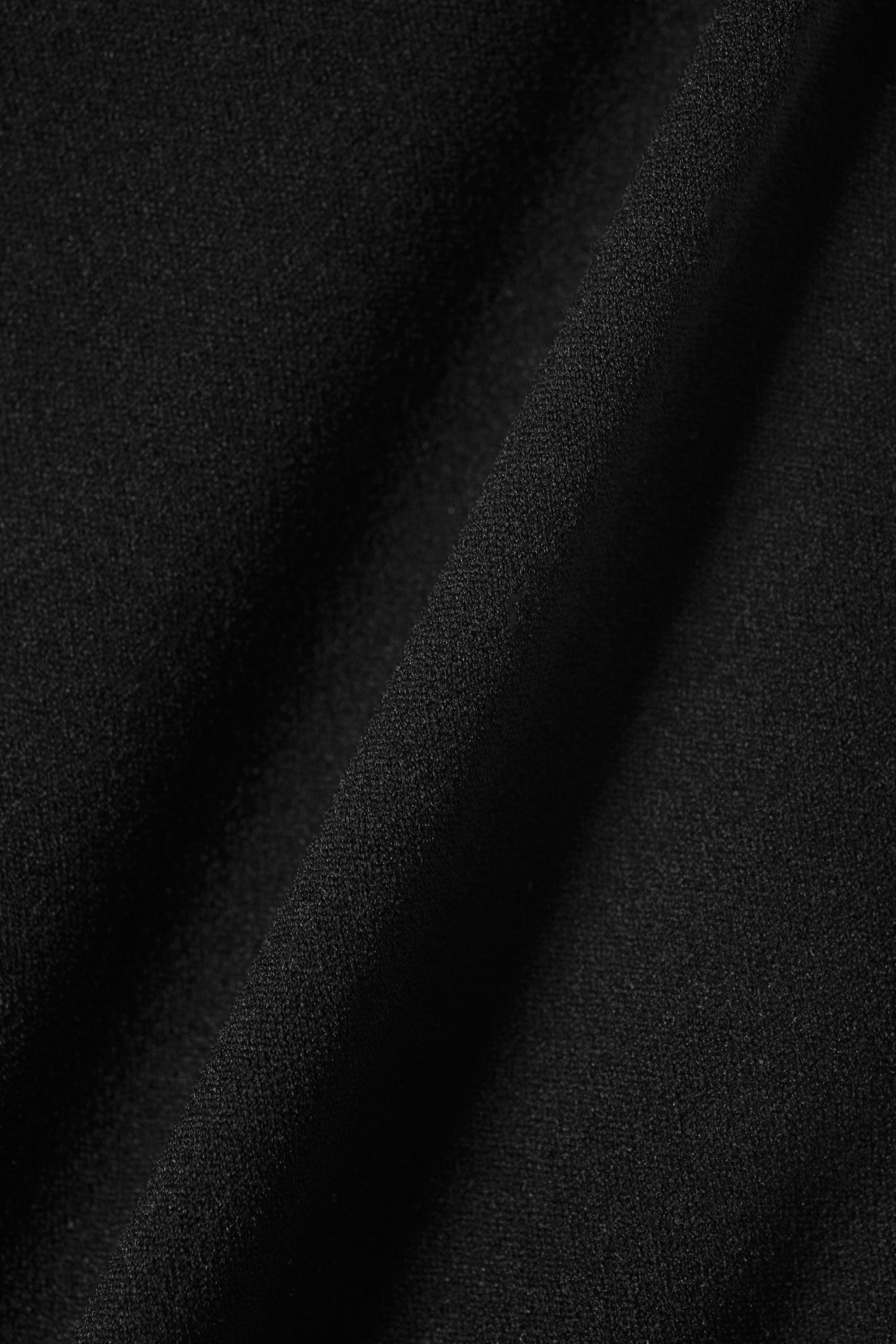 Grotere afbeelding bekijken: Zwarte stof vertoont een subtiele, kiezelachtige textuur met zachte plooien en draperieën.