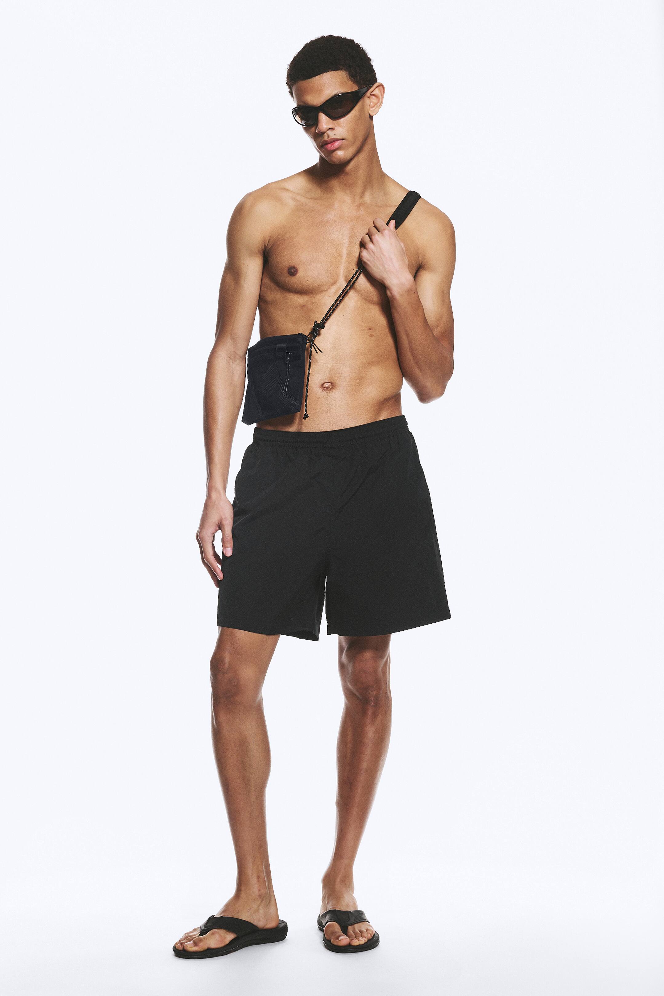 Ver imagen más grande: Pantalones cortos negros con cintura elástica y un ajuste relajado, que se extienden hasta la mitad del muslo. Se muestran desde un ángulo frontal, apareciendo en un tejido liso y tejido.