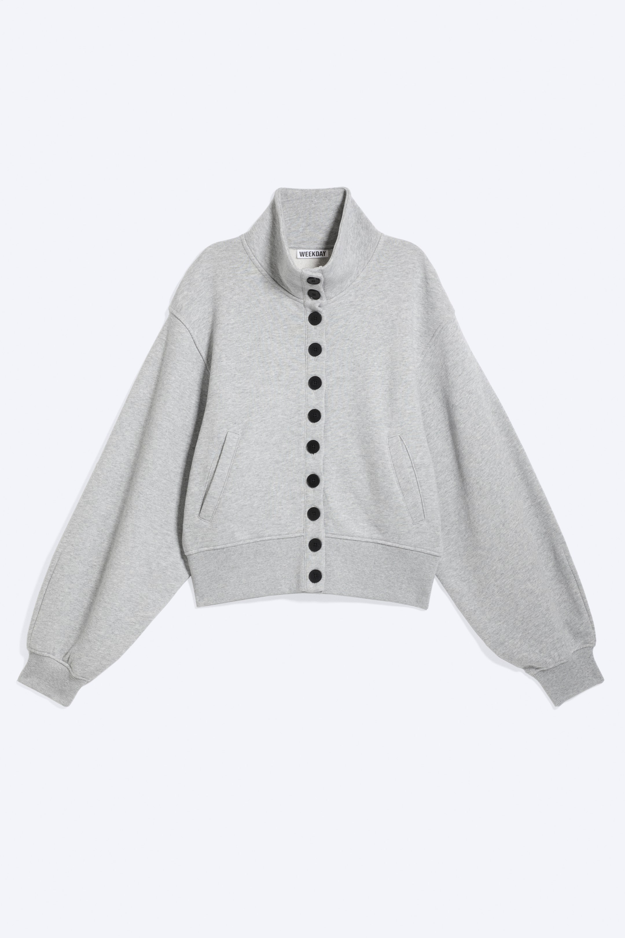 View larger image: A light grey sweatshirt jacket is laid flat, front facing, featuring a high stand-up collar and a vertical row of ten black circular buttons down the front. It also showcases long, wide sleeves with ribbed cuffs, a ribbed hem, and two front slash pockets.