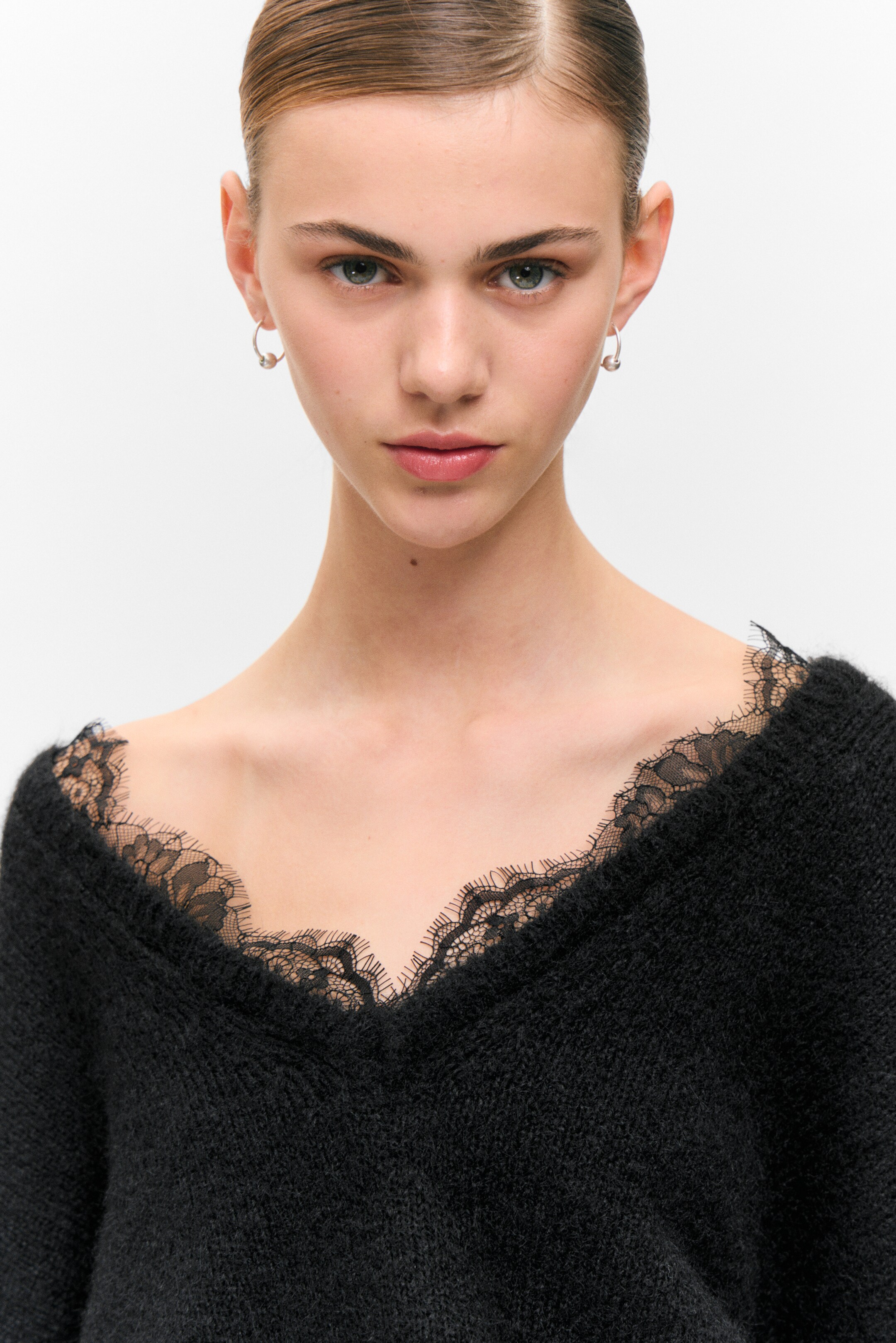 Visualizza immagine più grande: Un top nero in maglia pelosa presenta una profonda scollatura a V. La sua scollatura è delineata da un intricato bordo in pizzo nero.