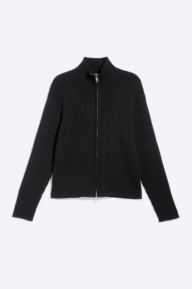 A black ribbed knit full-zip cardigan is showcased from the front. It features a stand-up collar, long sleeves, and a chunky silver-toned zip running down the centre. - 1