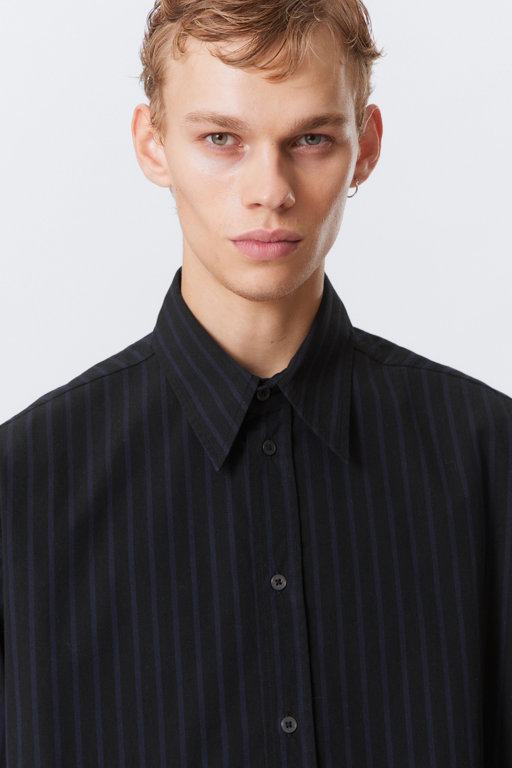 Ver imagen más grande: Una camisa negra abotonada presenta finas rayas verticales de color azul oscuro. Tiene un cuello en punta y botones redondos y oscuros en la tapeta delantera.